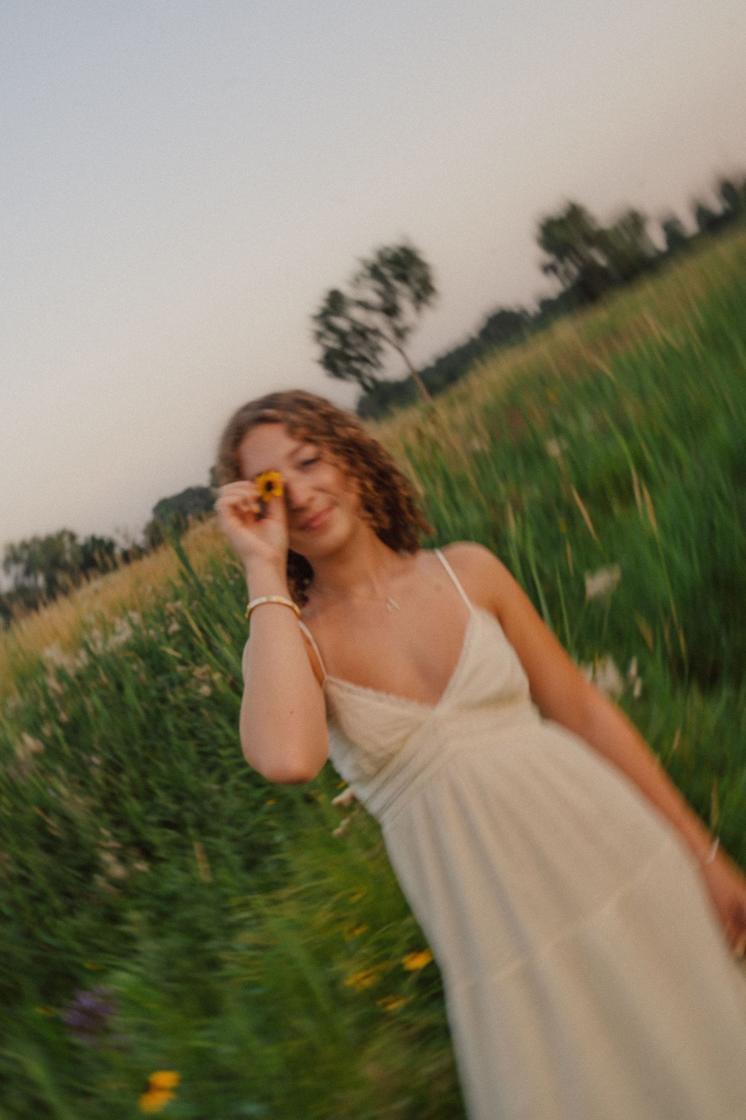 Someone in a white summer dress poses carefree in a green field during golden hour.