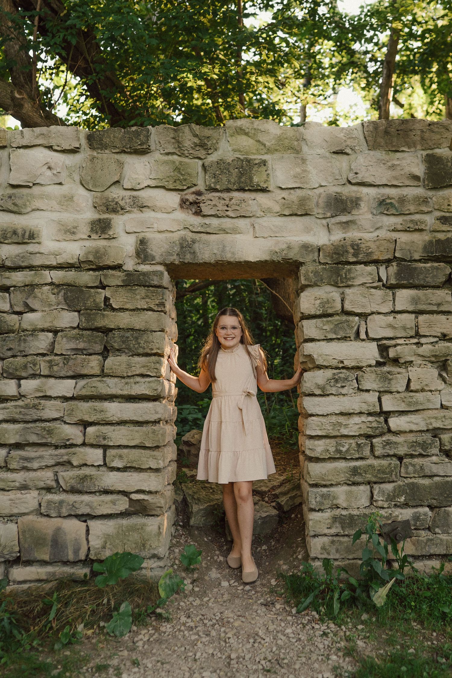 Young children play around old stone walls in light colored dresses creating a whimsical scene.