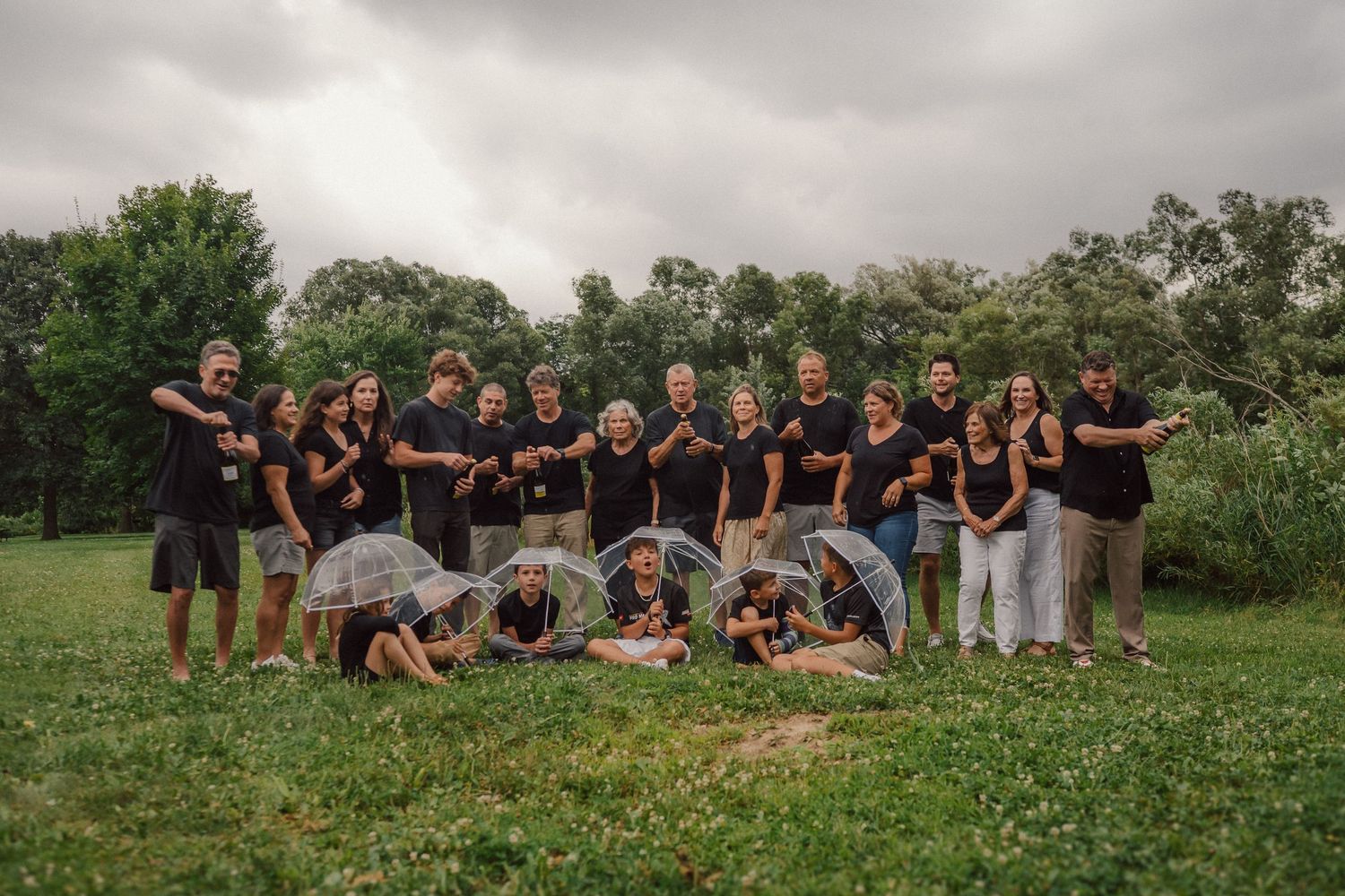 Large group photo of people in matching black shirts sitting together on grassy hill.
