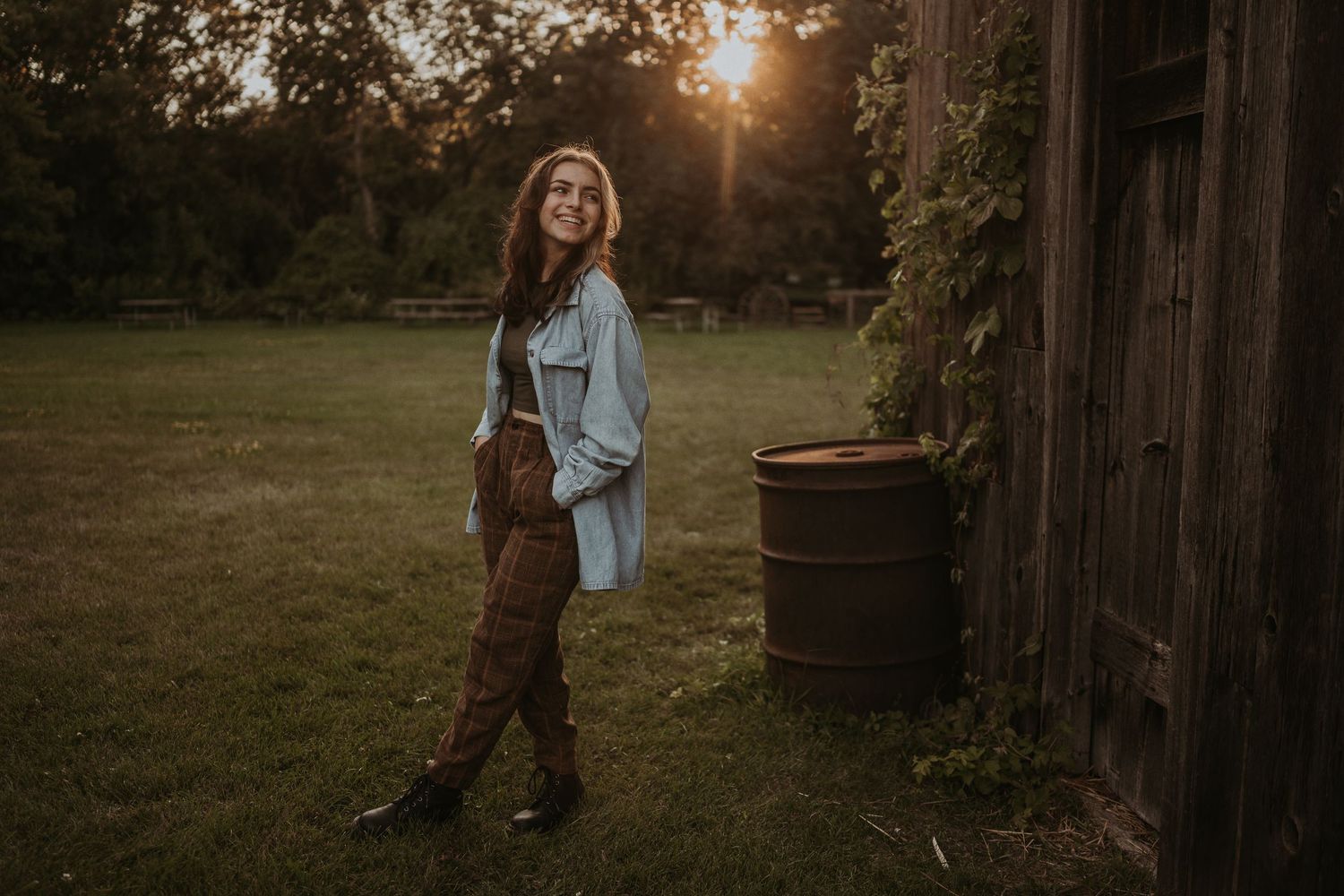 A person in casual attire poses near a rustic wooden barn at golden hour.
