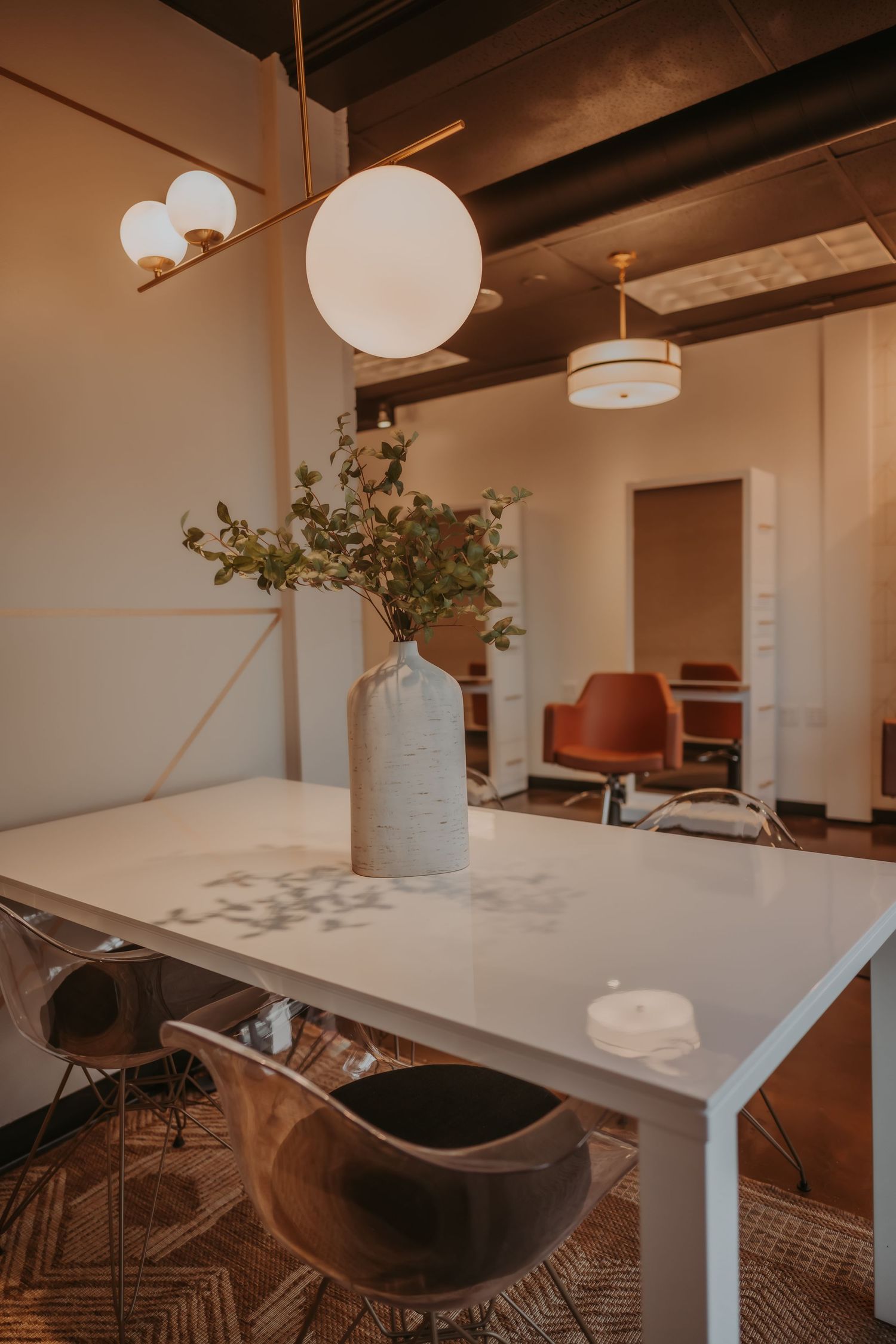 Modern office space with white table, globe pendant light, and decorative plant centerpiece.