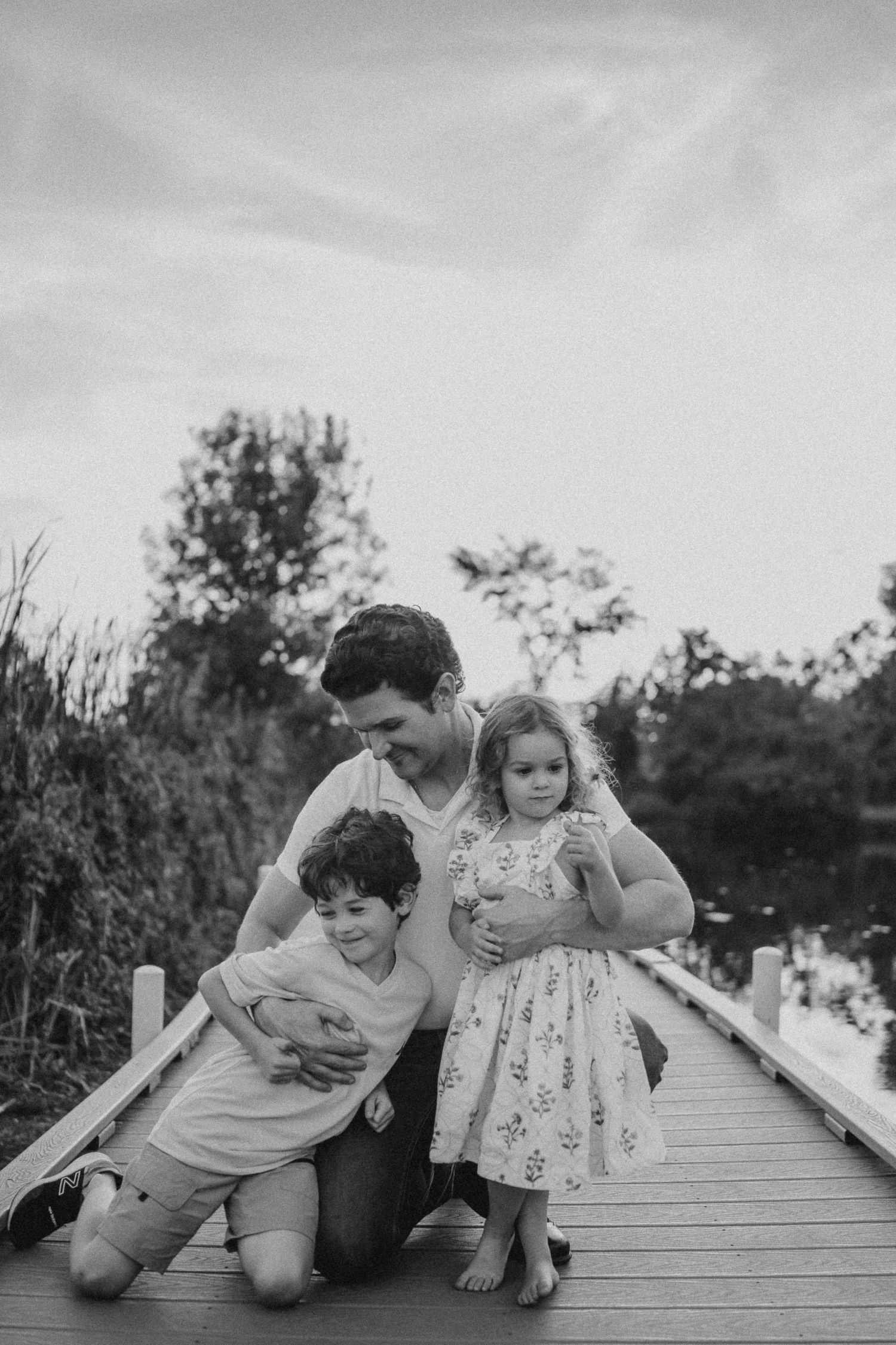 Black and white portrait of family sharing playful moments on a wooden boardwalk.