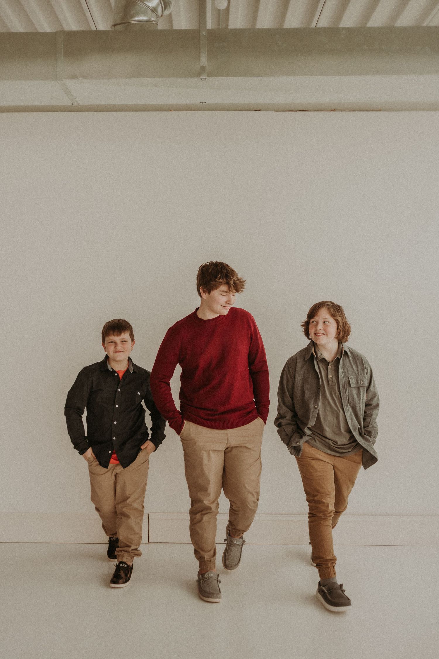 Three young people walking together in casual attire against a white studio backdrop.