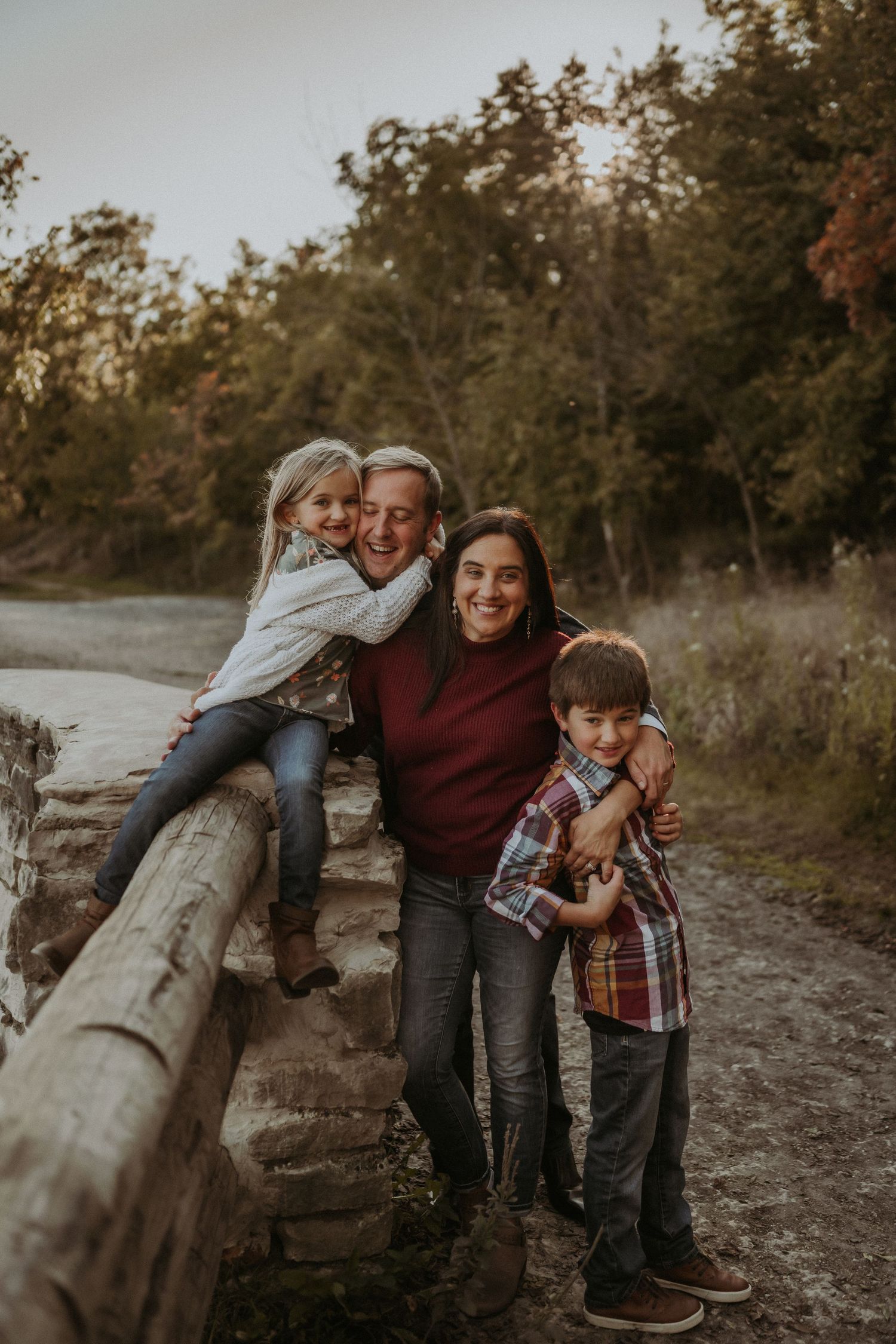 Family group poses playfully on rustic wooden fence during golden hour outdoor photoshoot.