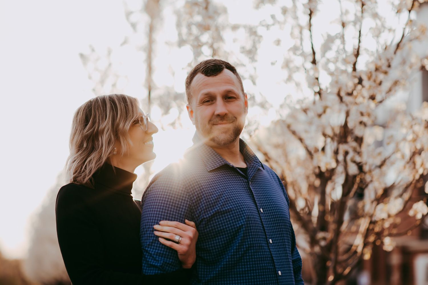 Couple shares intimate moment in sunlit outdoor setting with natural backdrop.