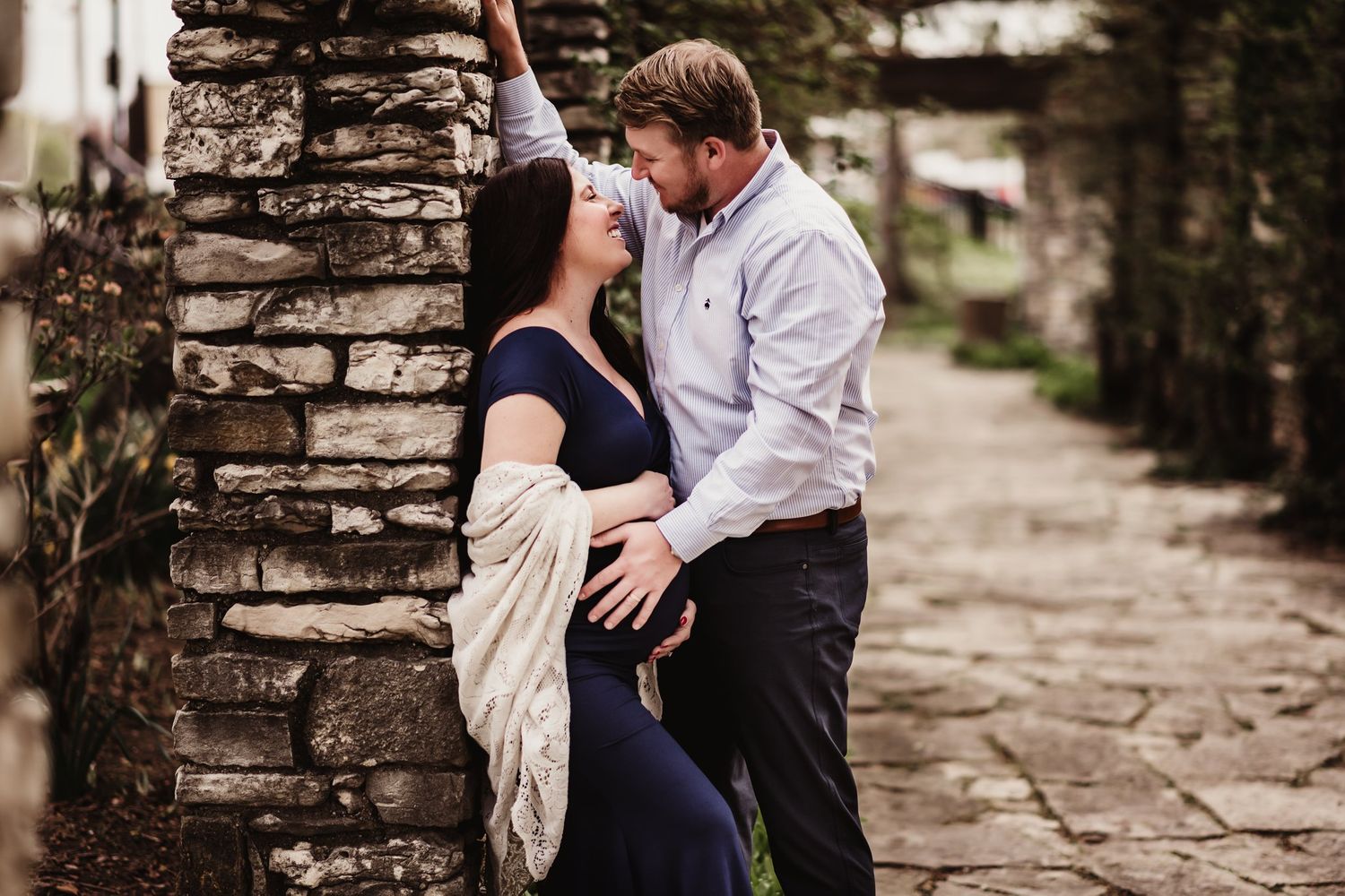 Romantic couple pose against stone pillar in garden pathway.