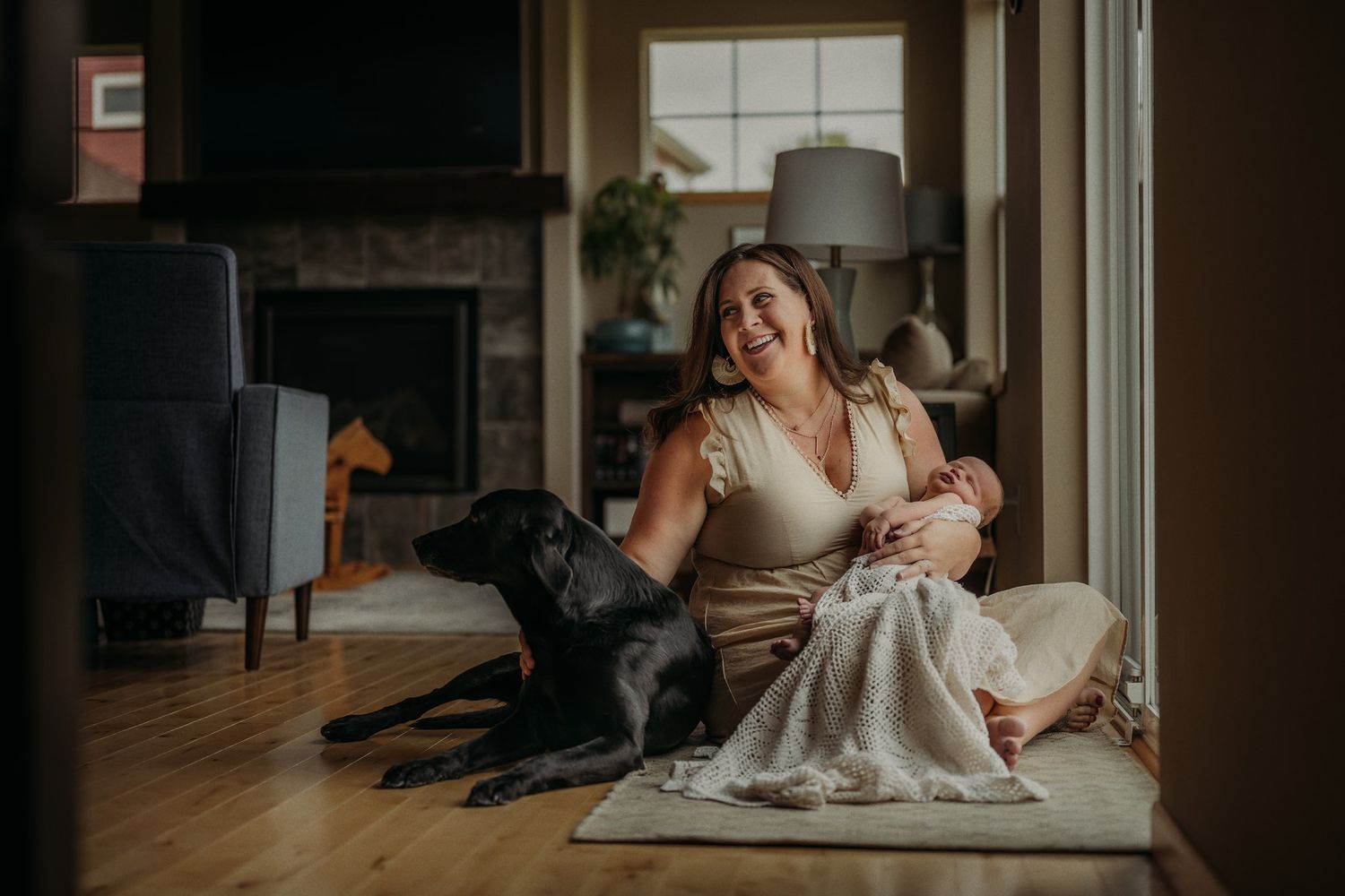 Cozy family scene with black dog and infant relaxing by window in natural light.