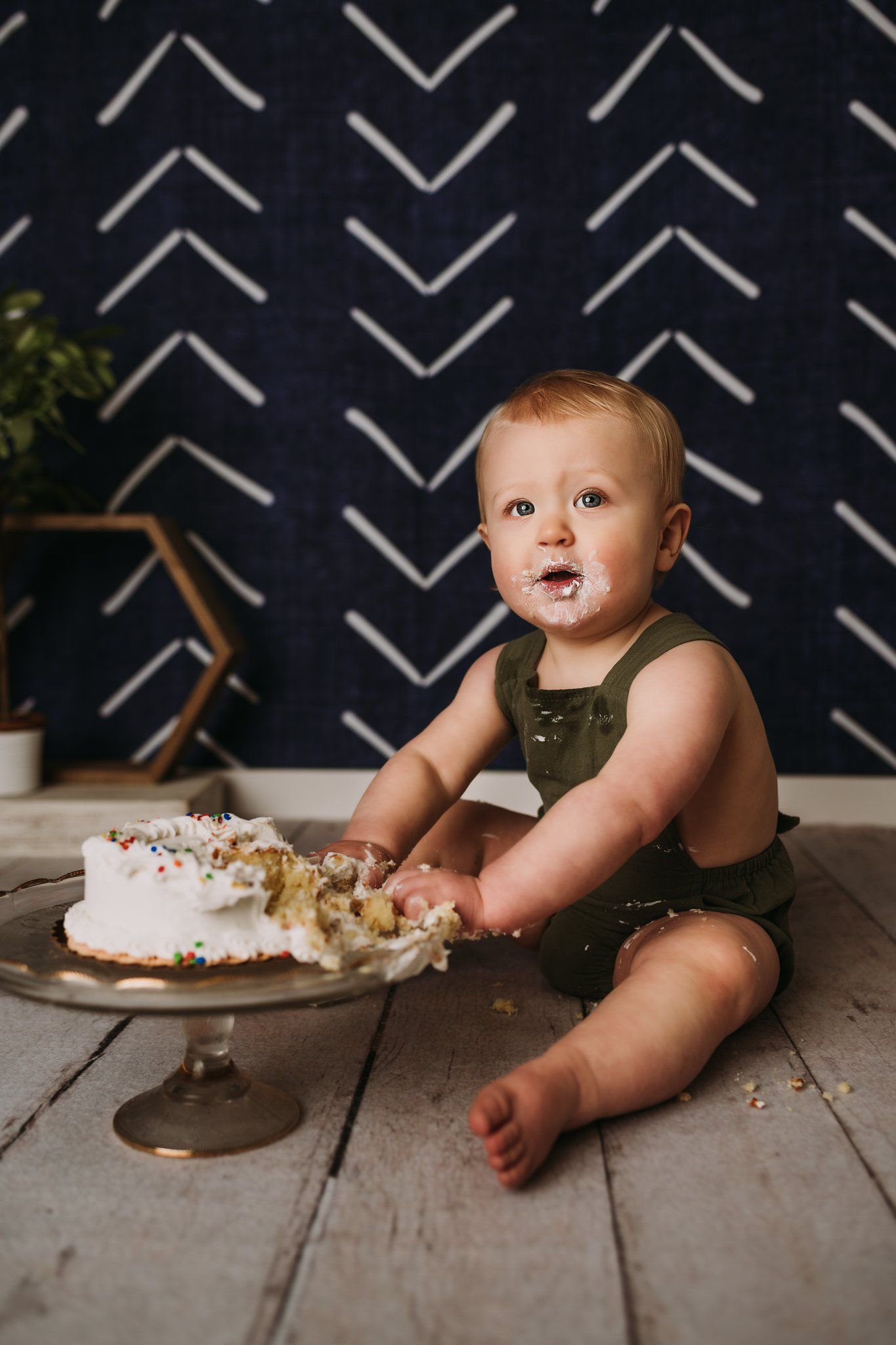 A cake smash photography session showing demolished white cake against navy patterned background.