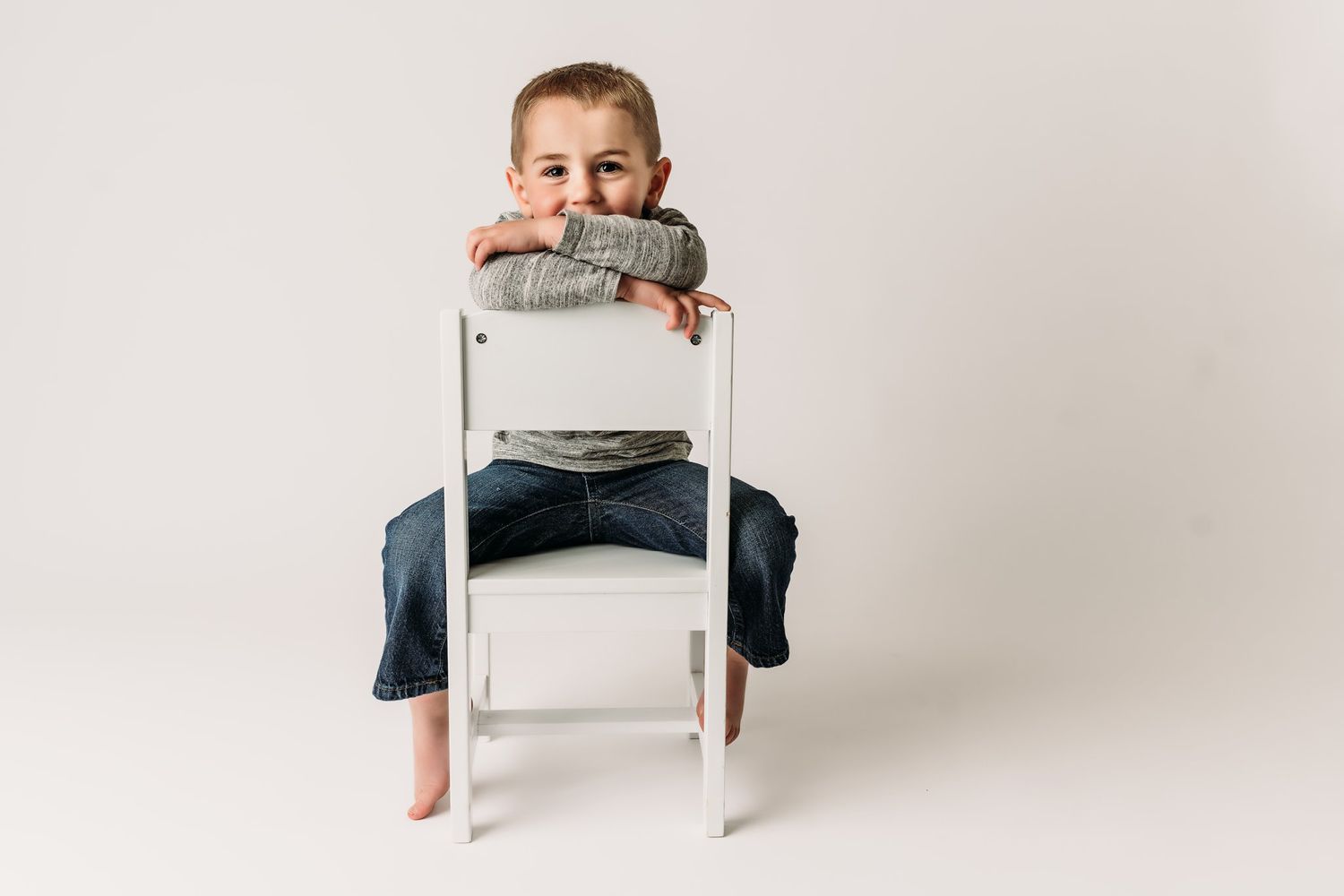 A casual portrait on a white chair showing playful expression in grey and denim.