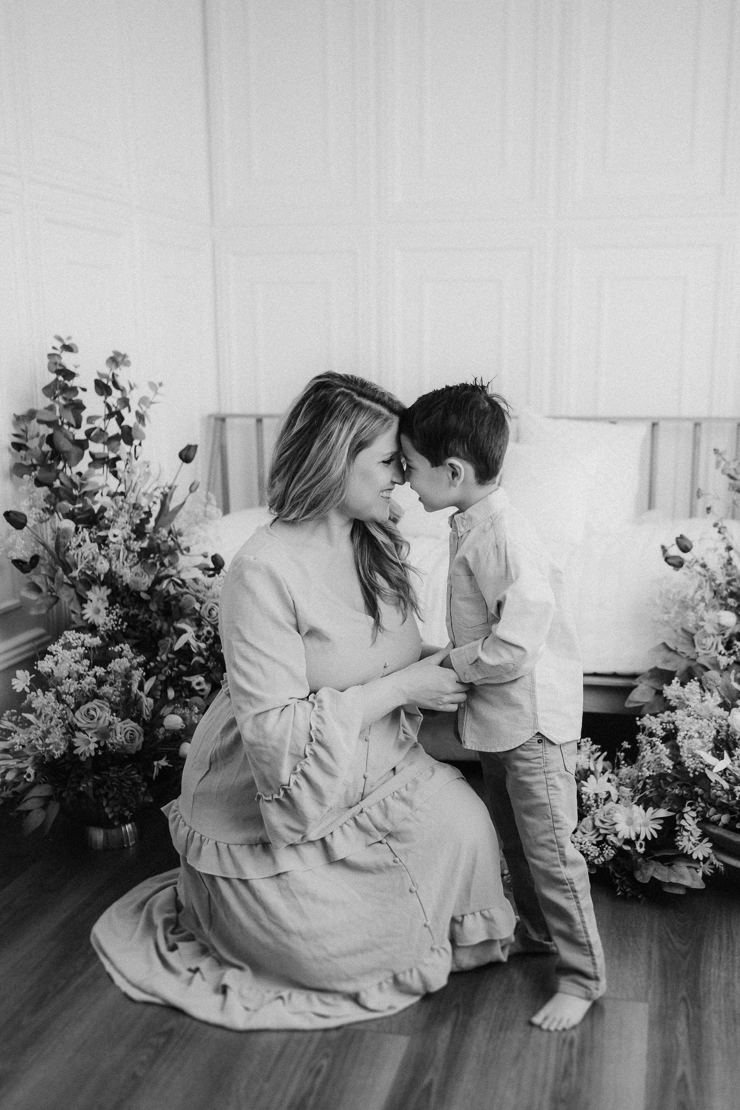 A tender black and white portrait of a bonding moment between mother and child surrounded by floral arrangements.