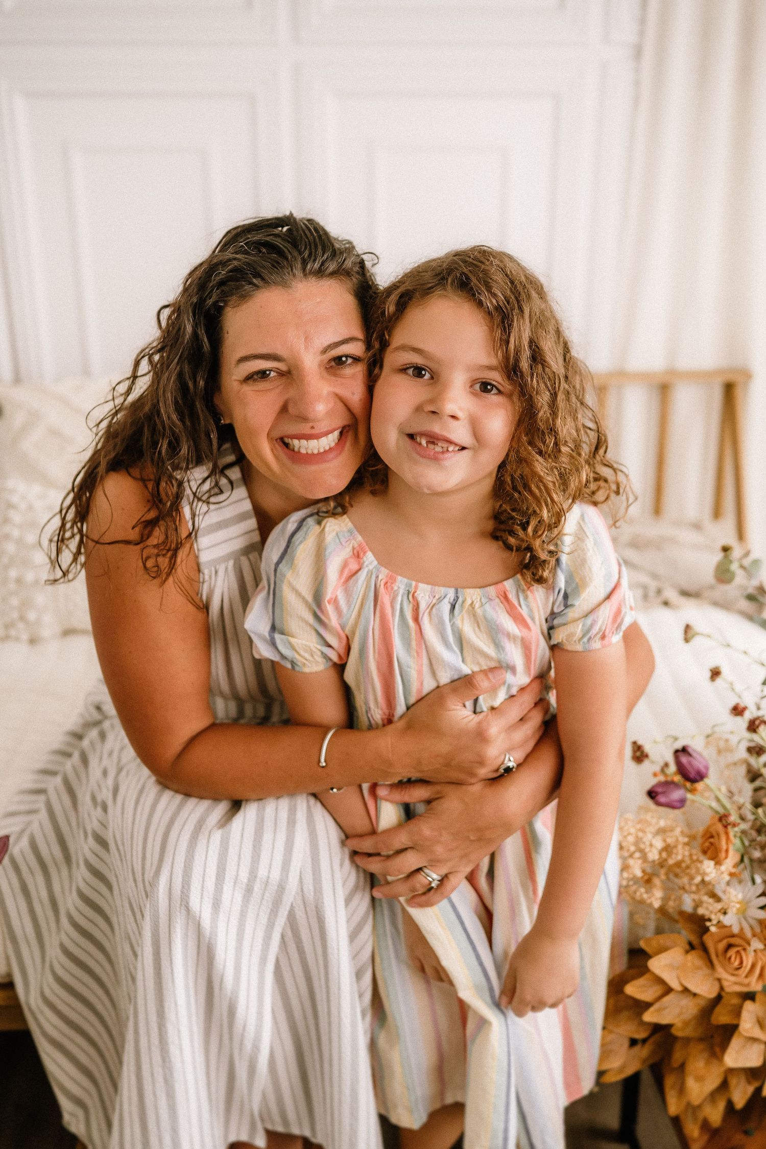 A heartwarming mother-daughter moment captured in a bright white room decorated with warm floral elements.
