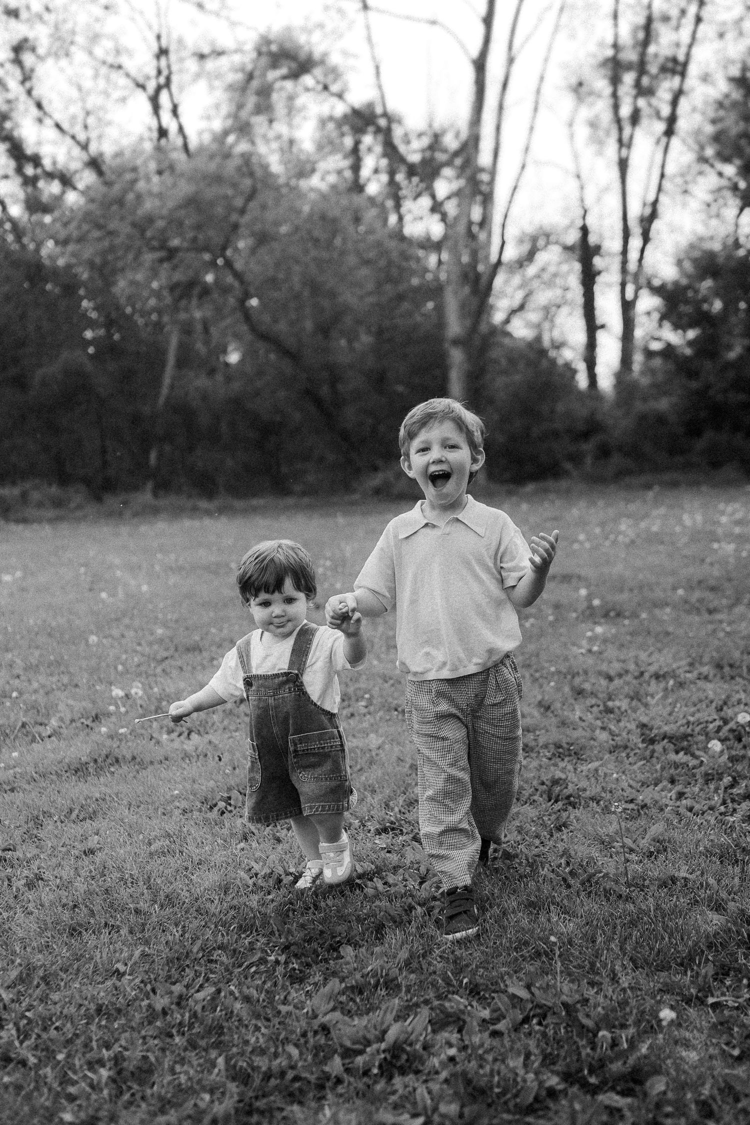 Two children playing and laughing together in a black and white photo taken in a grassy field.