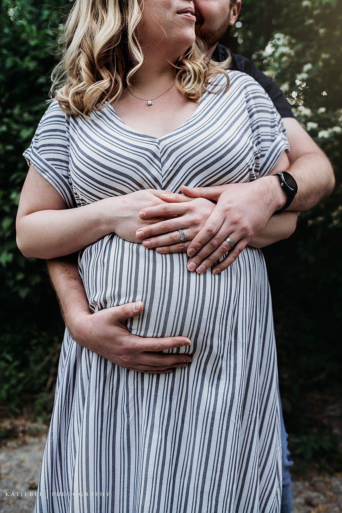 Close-up detail of hands cradling a baby bump in a striped maternity dress.