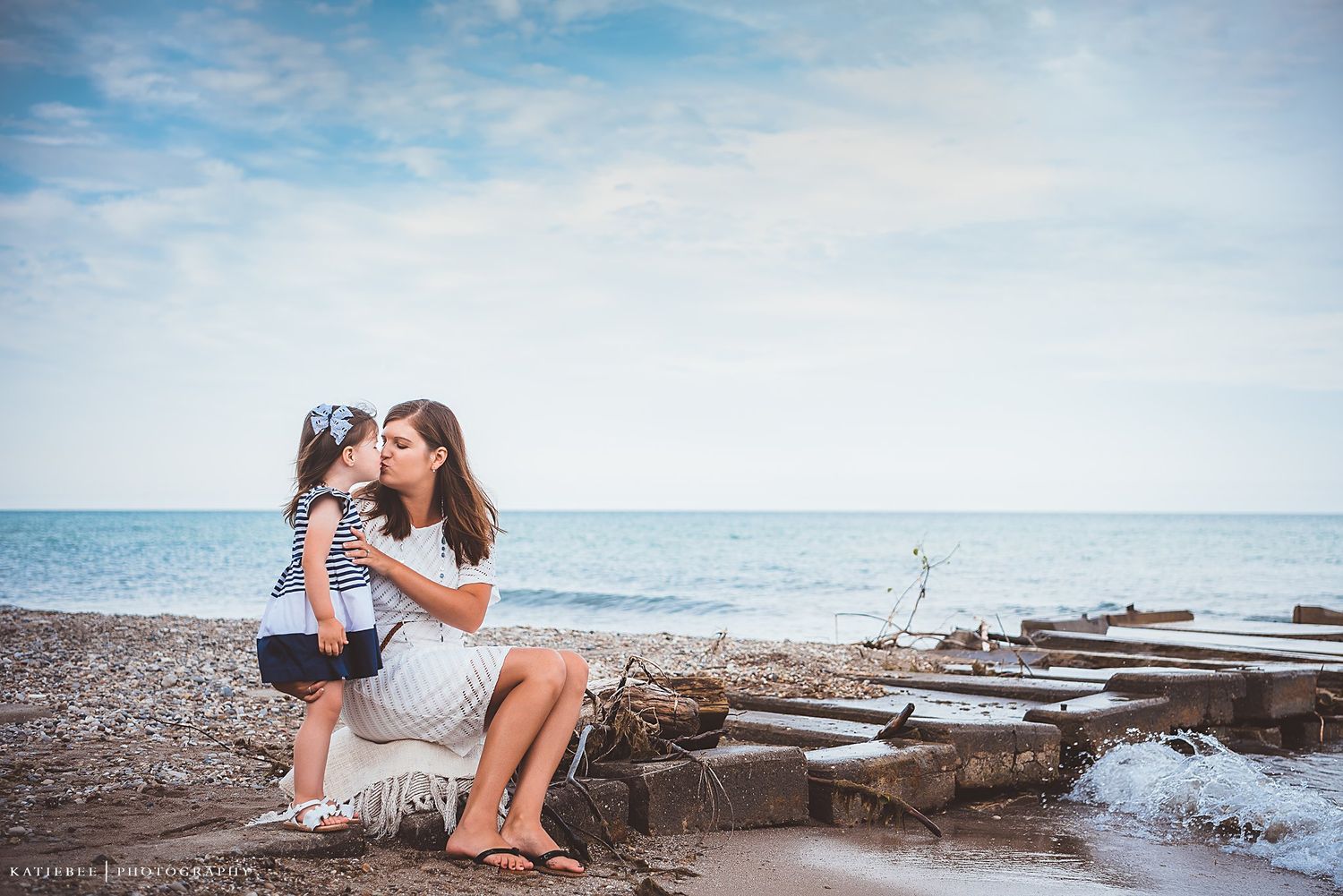 An intimate beachside portrait showing affection between parent and child on rocky shore.