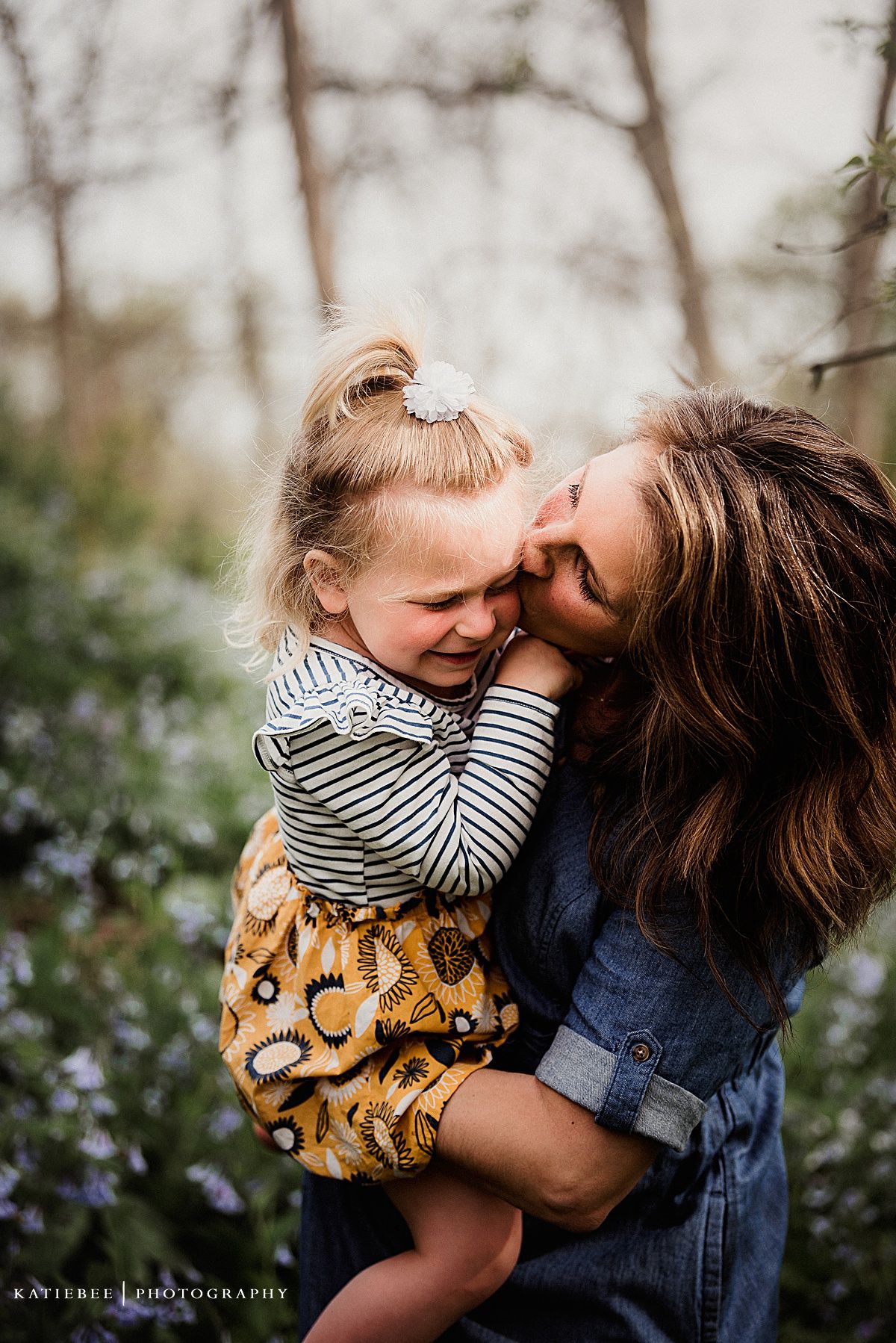 A joyful intimate moment captured in a wooded setting with purple flowers below.
