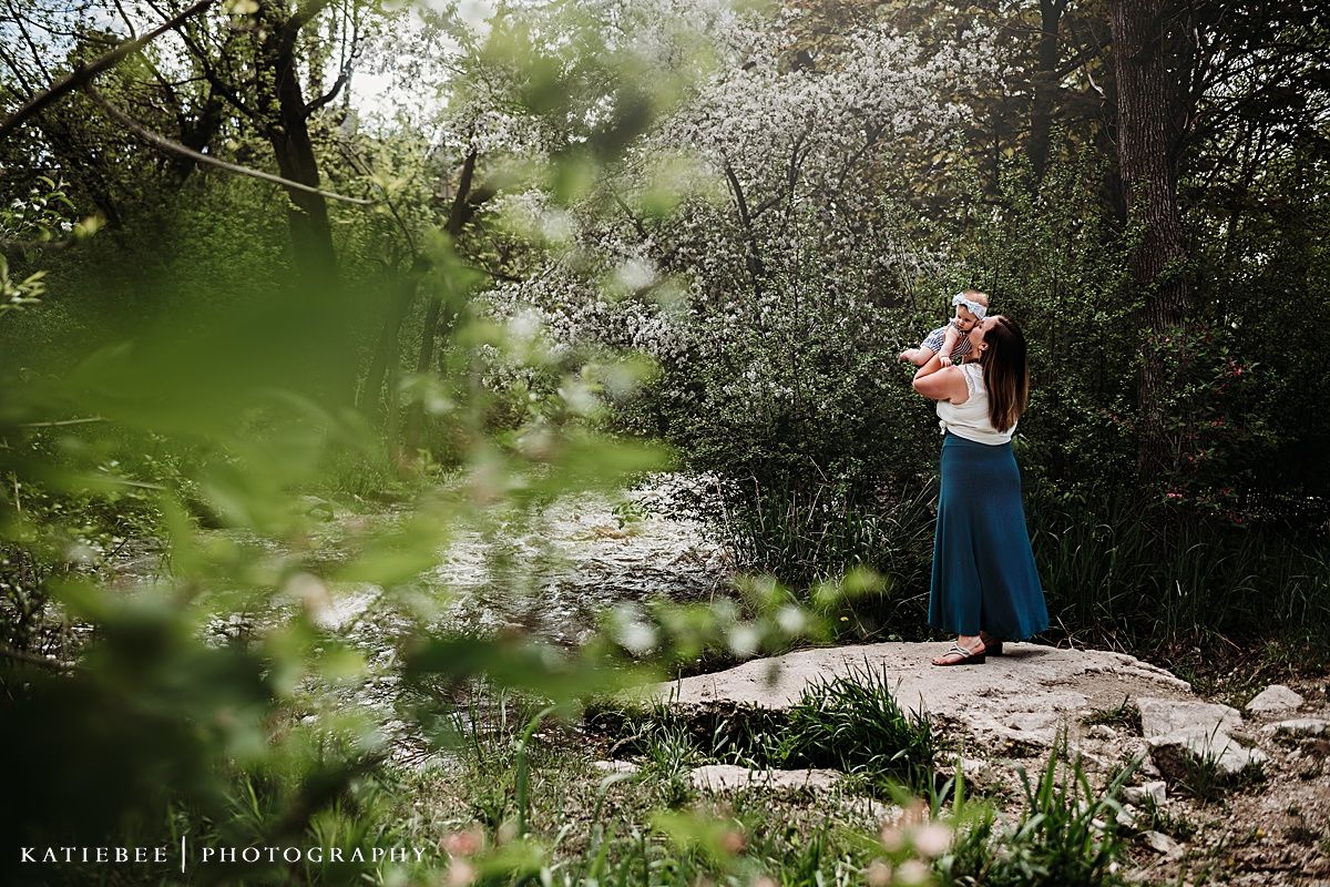 Person in blue skirt photographed through flowering branches on rocky outdoor terrain.
