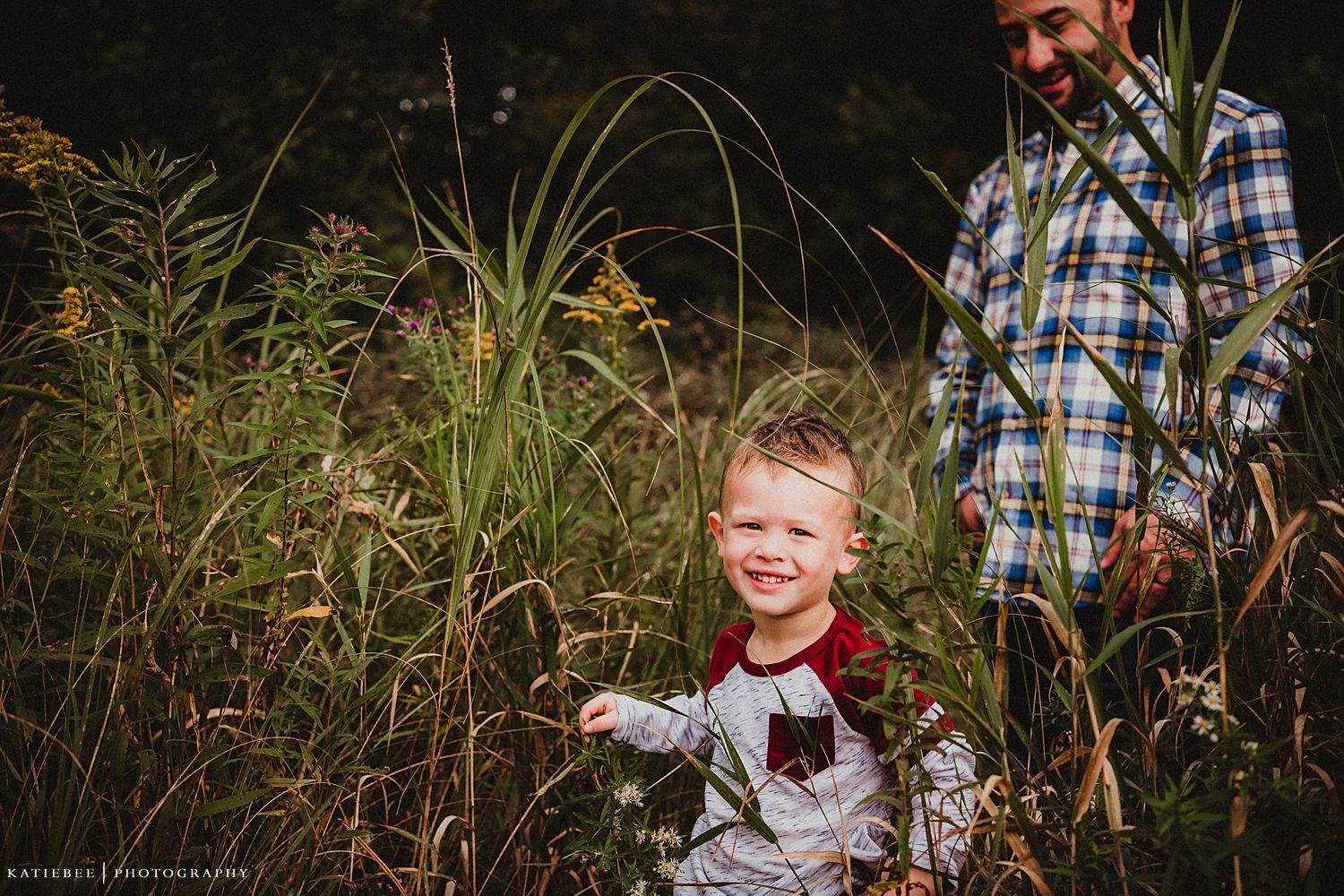 Young child and adult walking through tall grass and wildflowers.