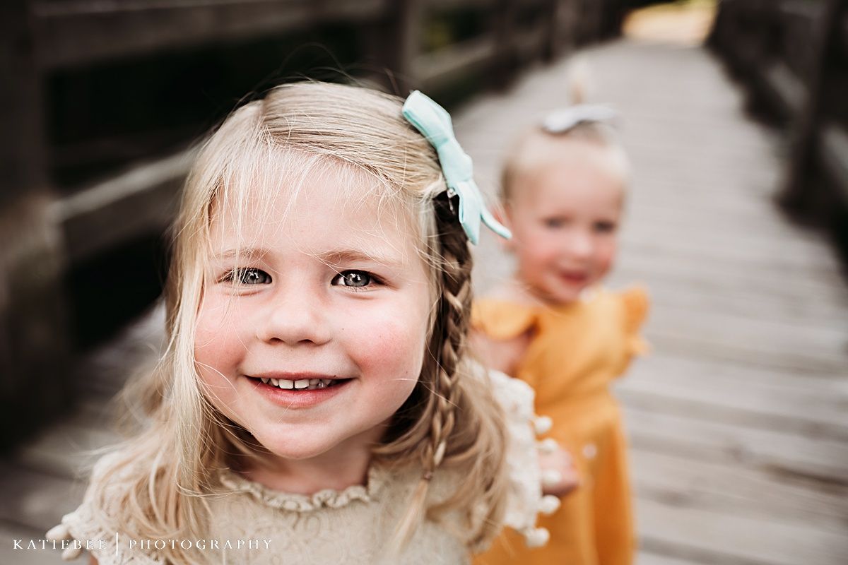 Two children smiling while playing on wooden bridge.