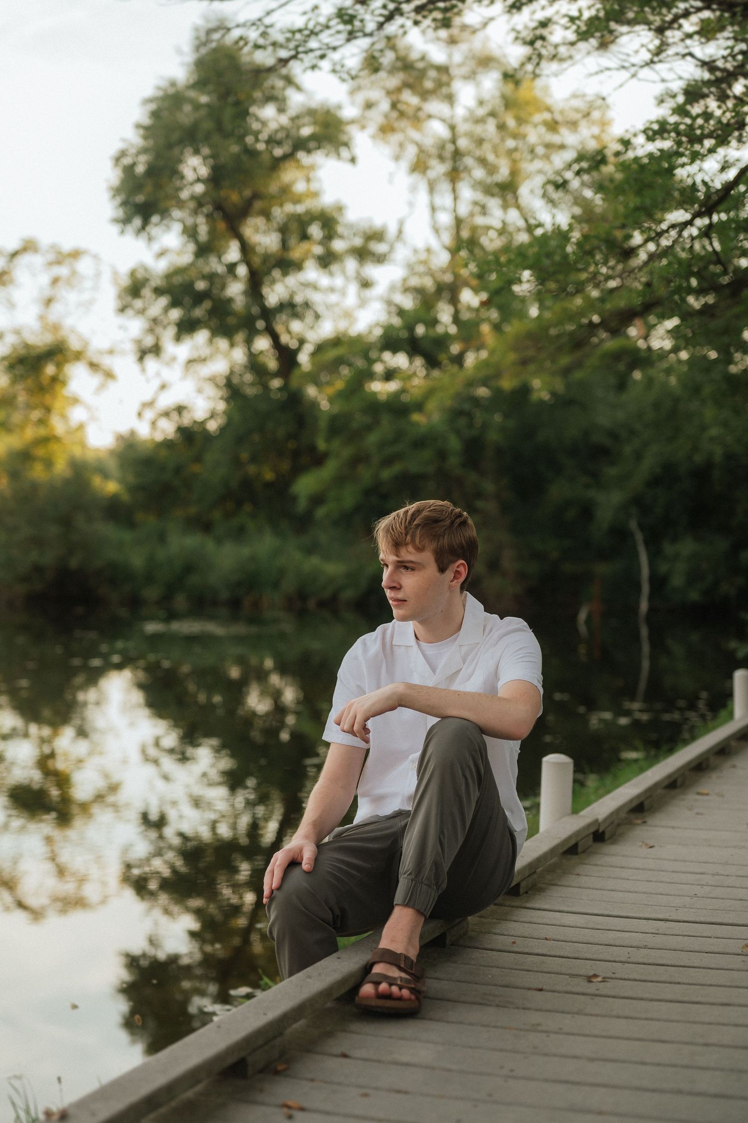 Person lounging on a wooden dock by a tranquil lake during sunset, creating a peaceful and reflective scene.