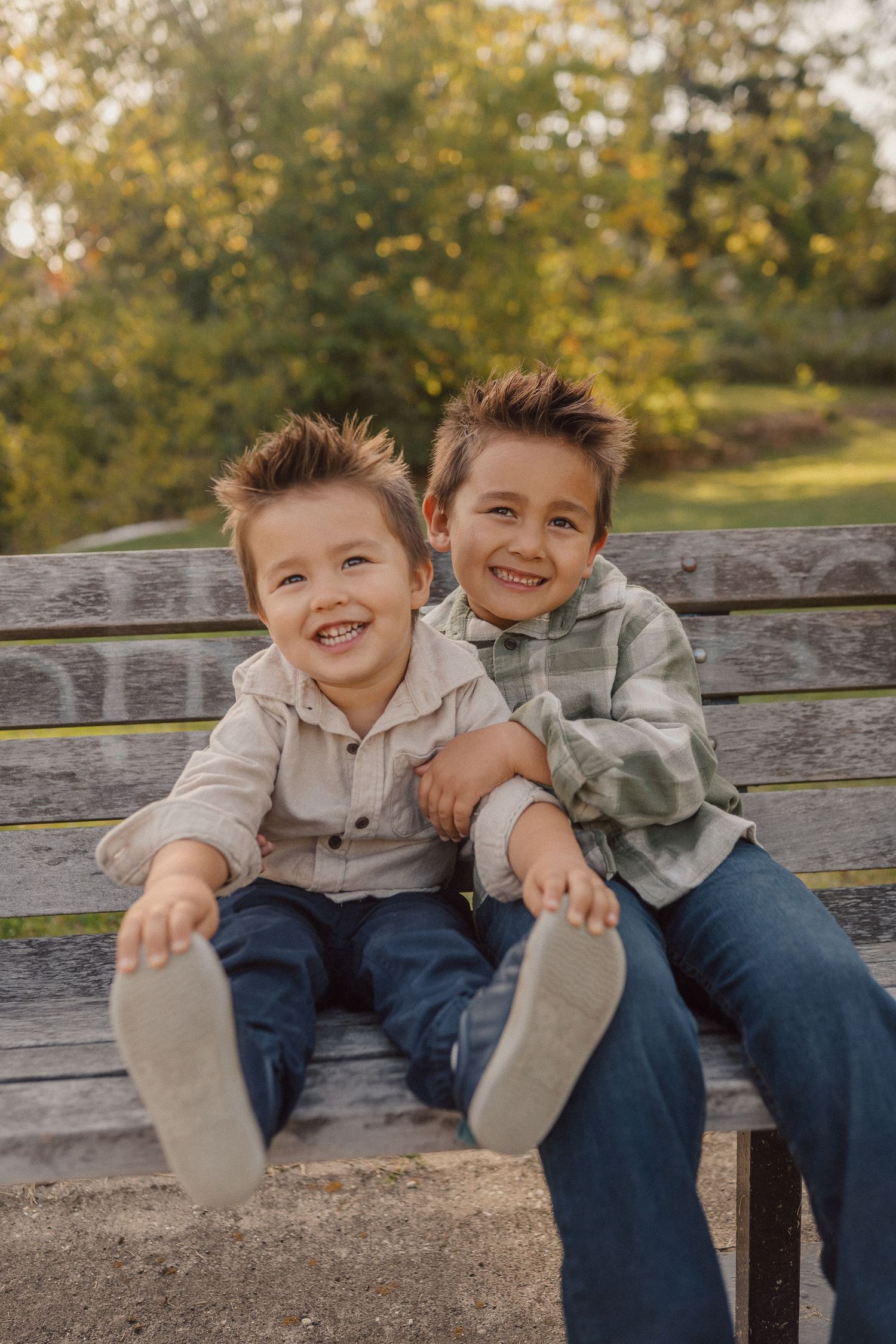 Two young children sit together on a wooden bench sharing laughs and playful moments.