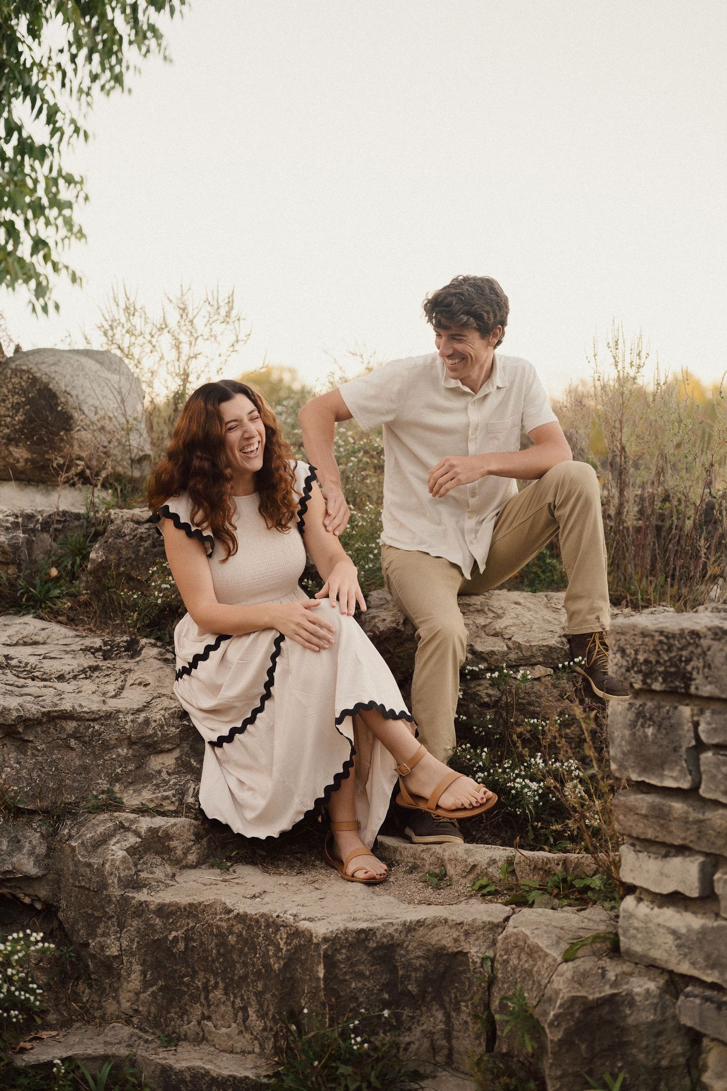 A couple shares intimate moments while sitting on a rustic stone wall during a romantic outdoor photo session at sunset.
