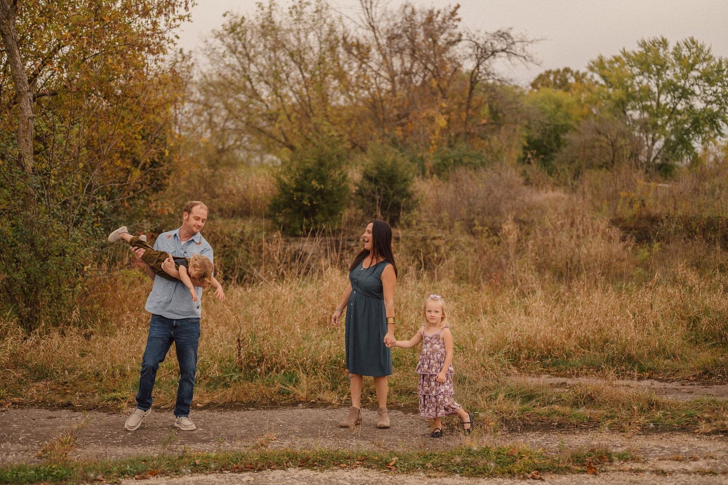 A family poses together in a natural setting during golden hour with fall foliage in background.