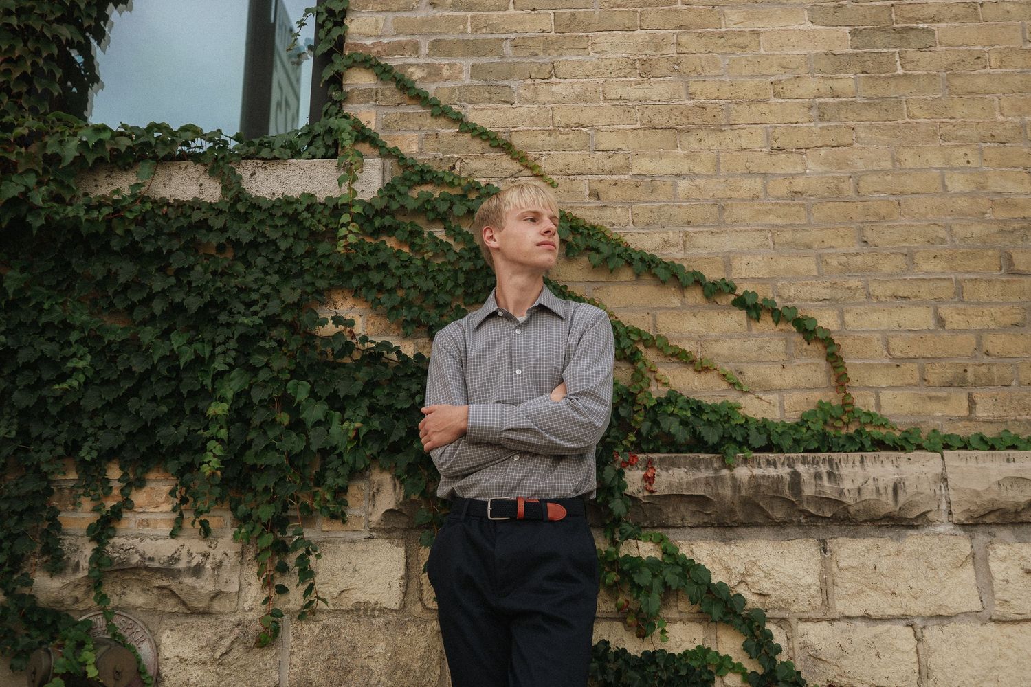 Person in gray polo shirt poses against a brick wall with climbing ivy vines.