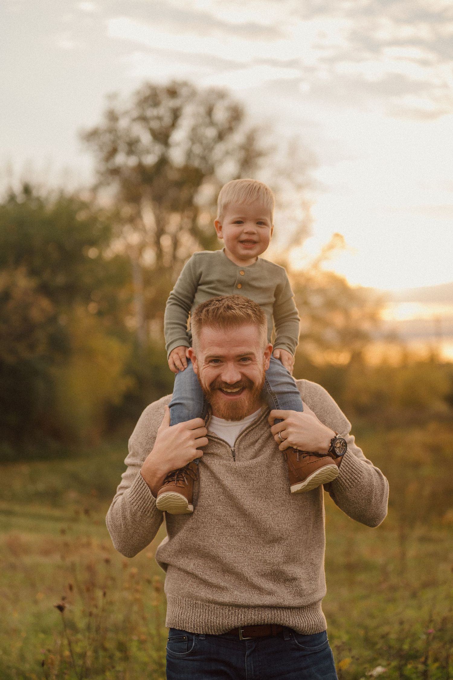 A heartwarming outdoor scene at sunset with a small child riding on shoulders in a grassy field.
