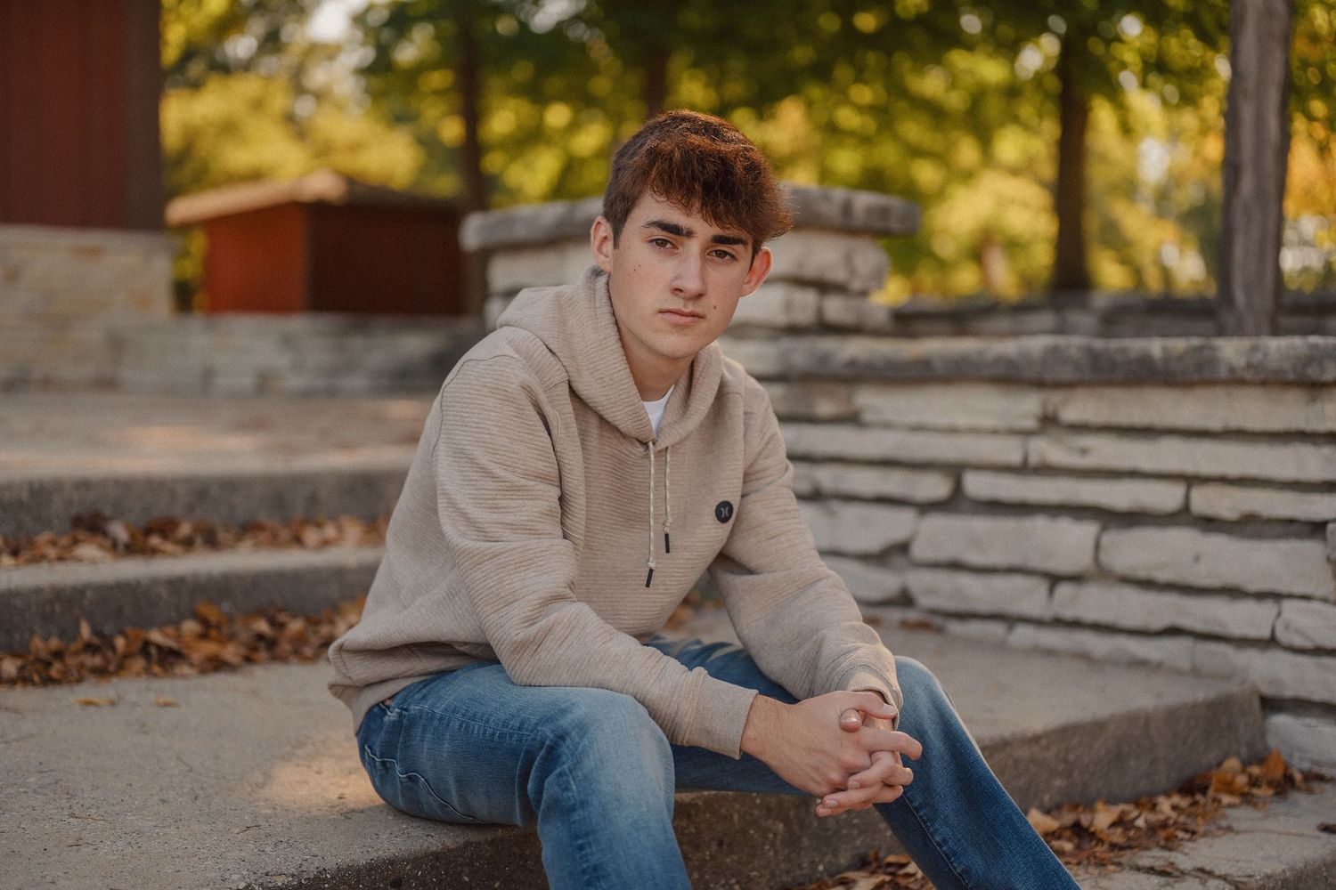 A person in a beige hoodie and jeans sits on stone steps during golden hour.
