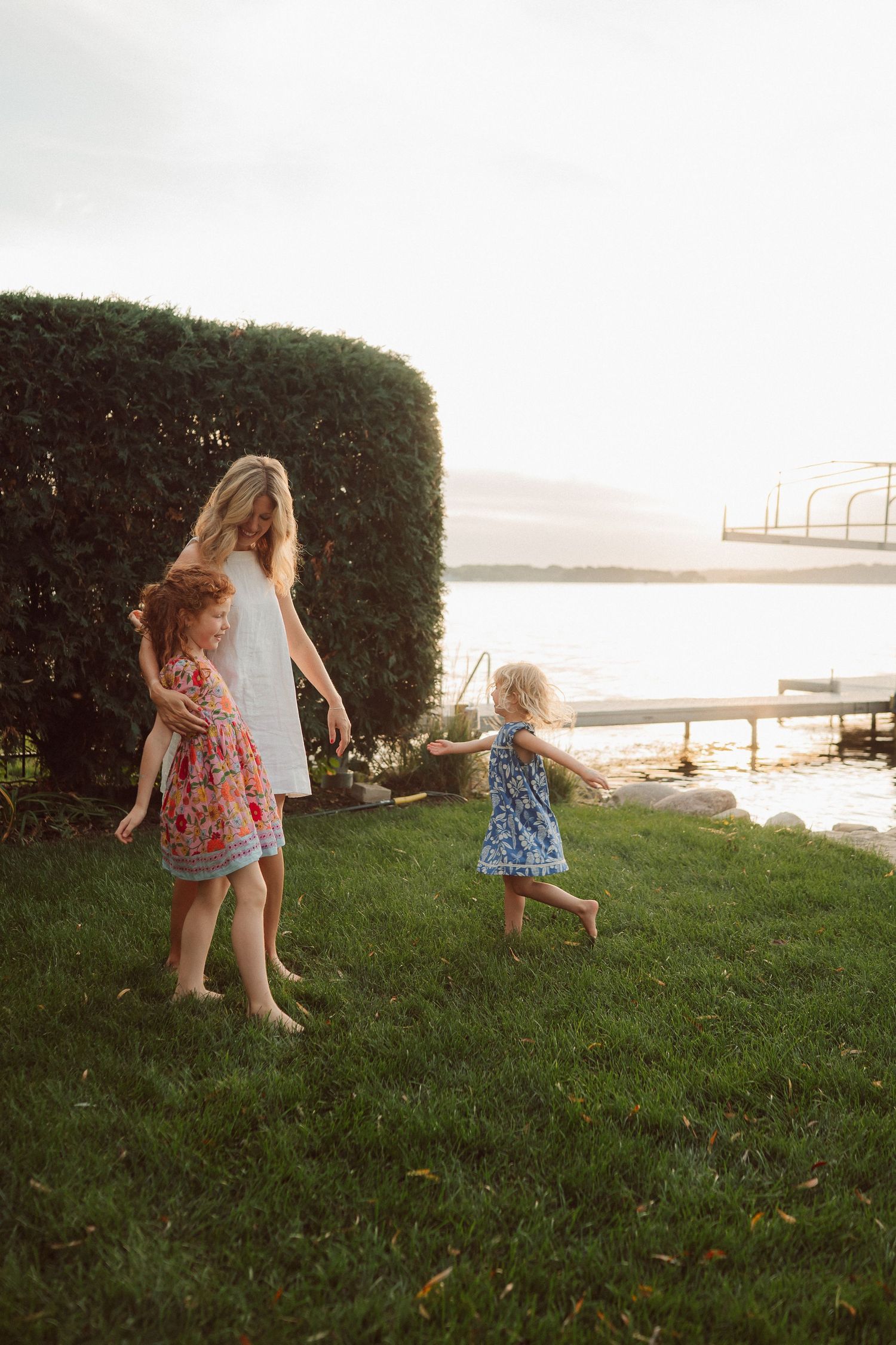 Children running and playing on a grassy hillside near the water during golden hour.