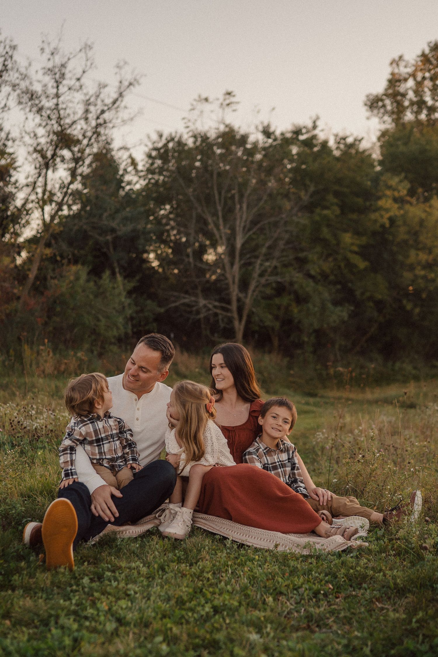 Family relaxing together on a blanket in a rustic field during golden hour sunset.