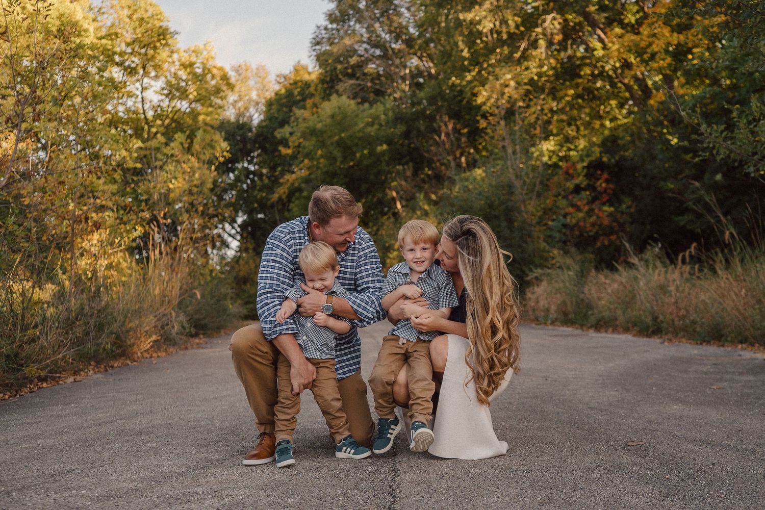 A family shares a tender moment together on a sunlit path surrounded by autumn foliage.