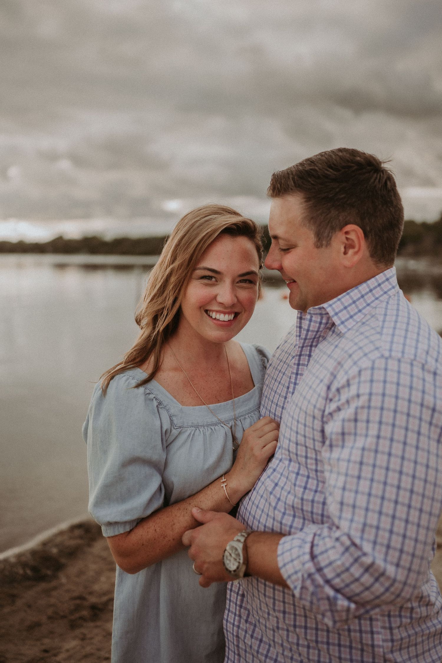 A couple shares an intimate moment on the beach with dramatic clouds overhead.