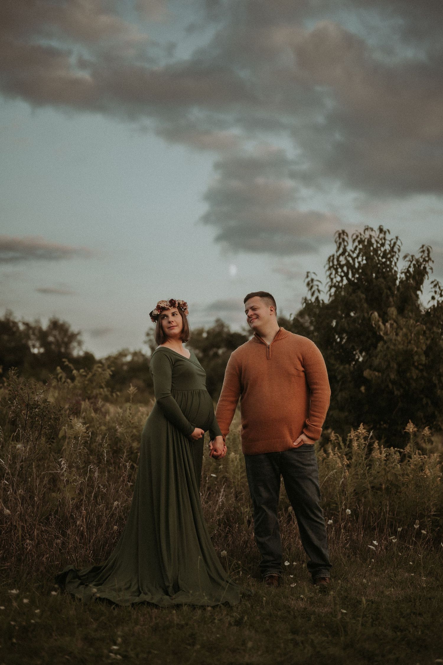 A couple poses together in a field at sunset wearing coordinating autumn colors.