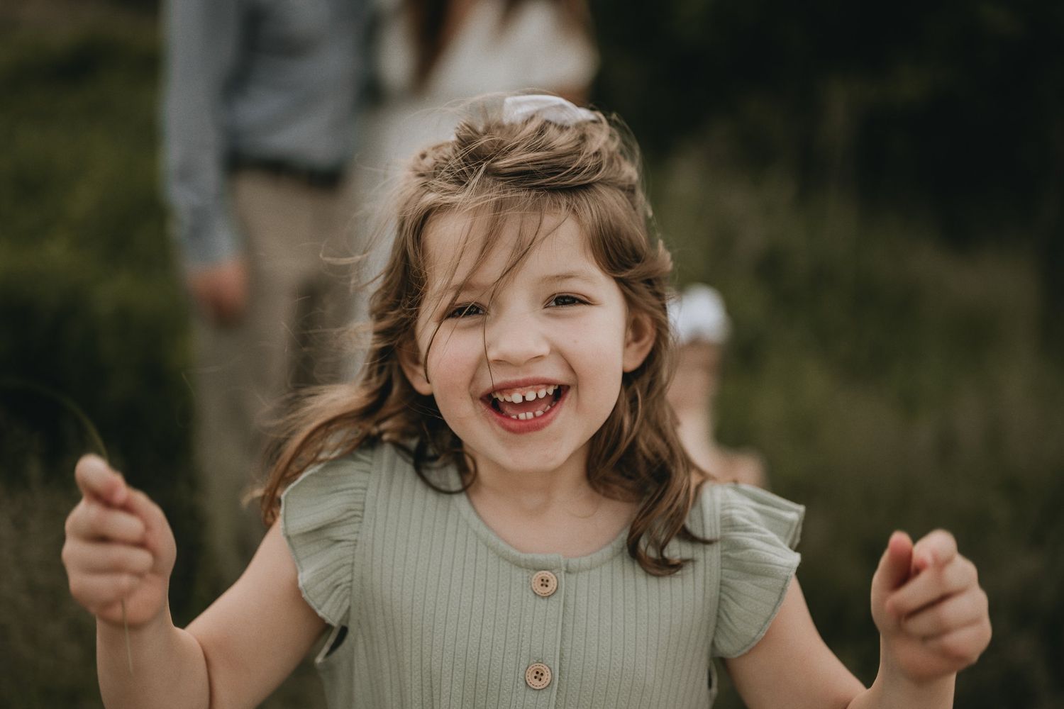 Close-up portrait of a laughing child wearing a sage green dress with ruffled sleeves outdoors.