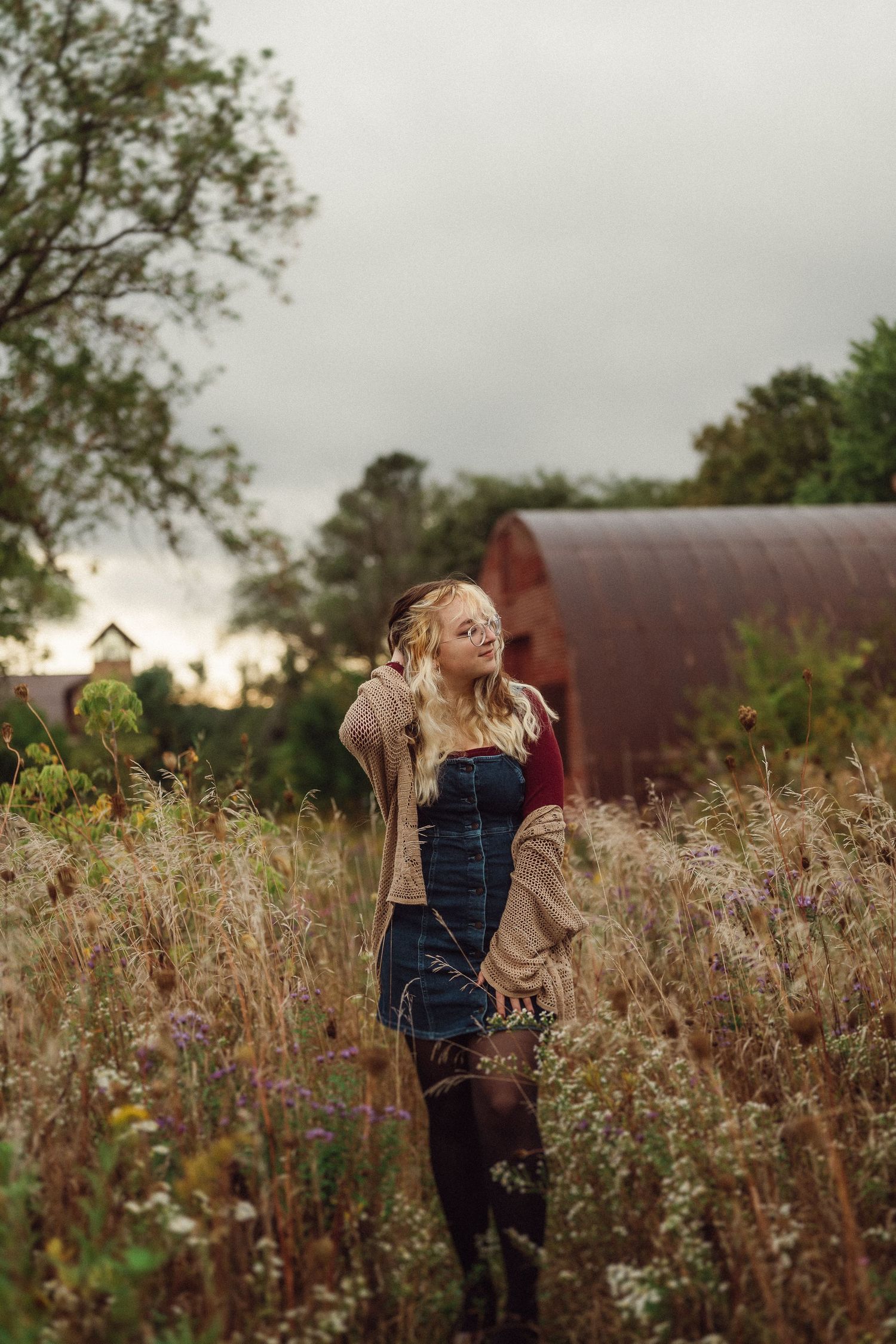 Dreamy autumn portrait in a wildflower meadow with moody overcast sky and red barn in background.