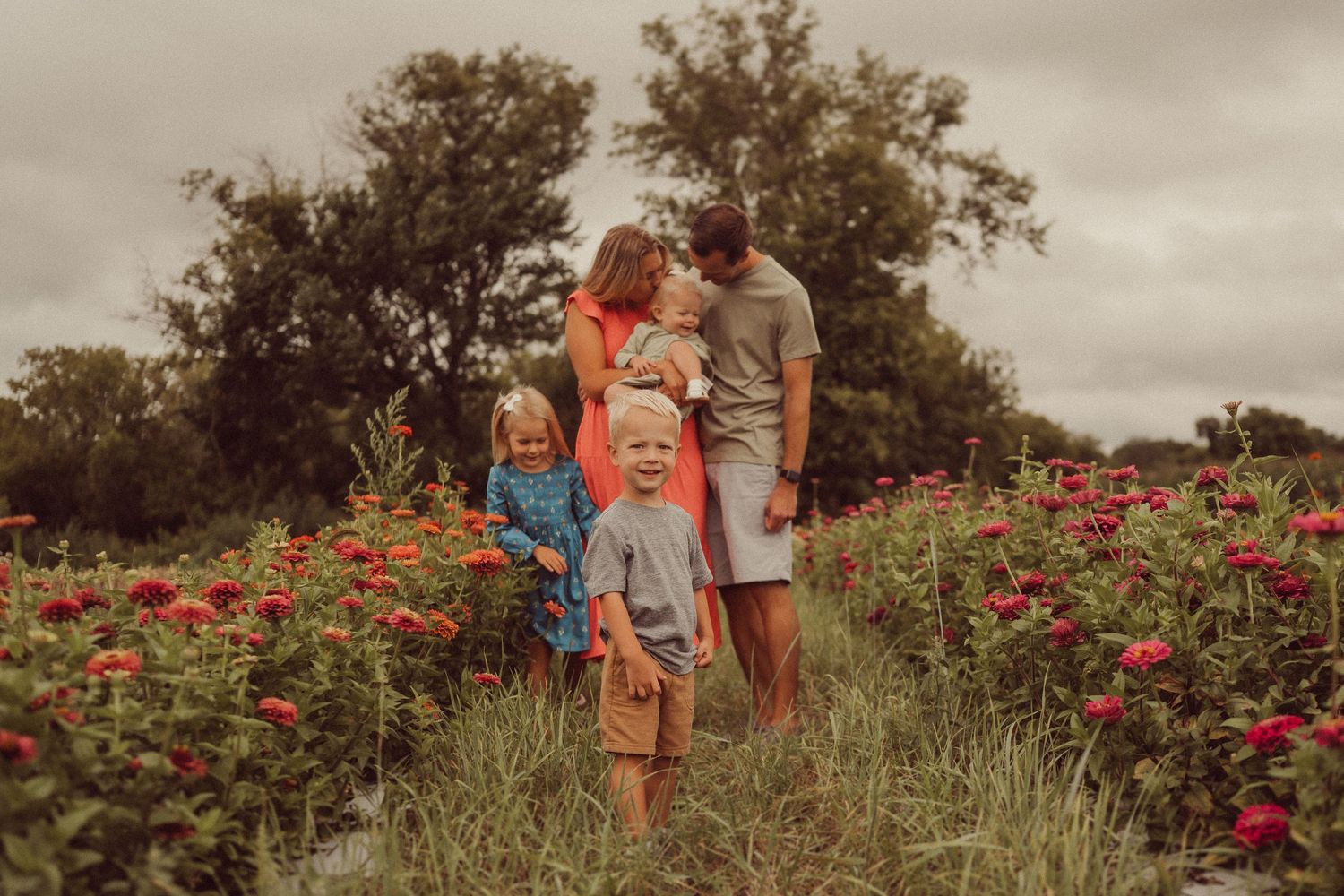 Family standing together in a vibrant field of red flowers during sunset.