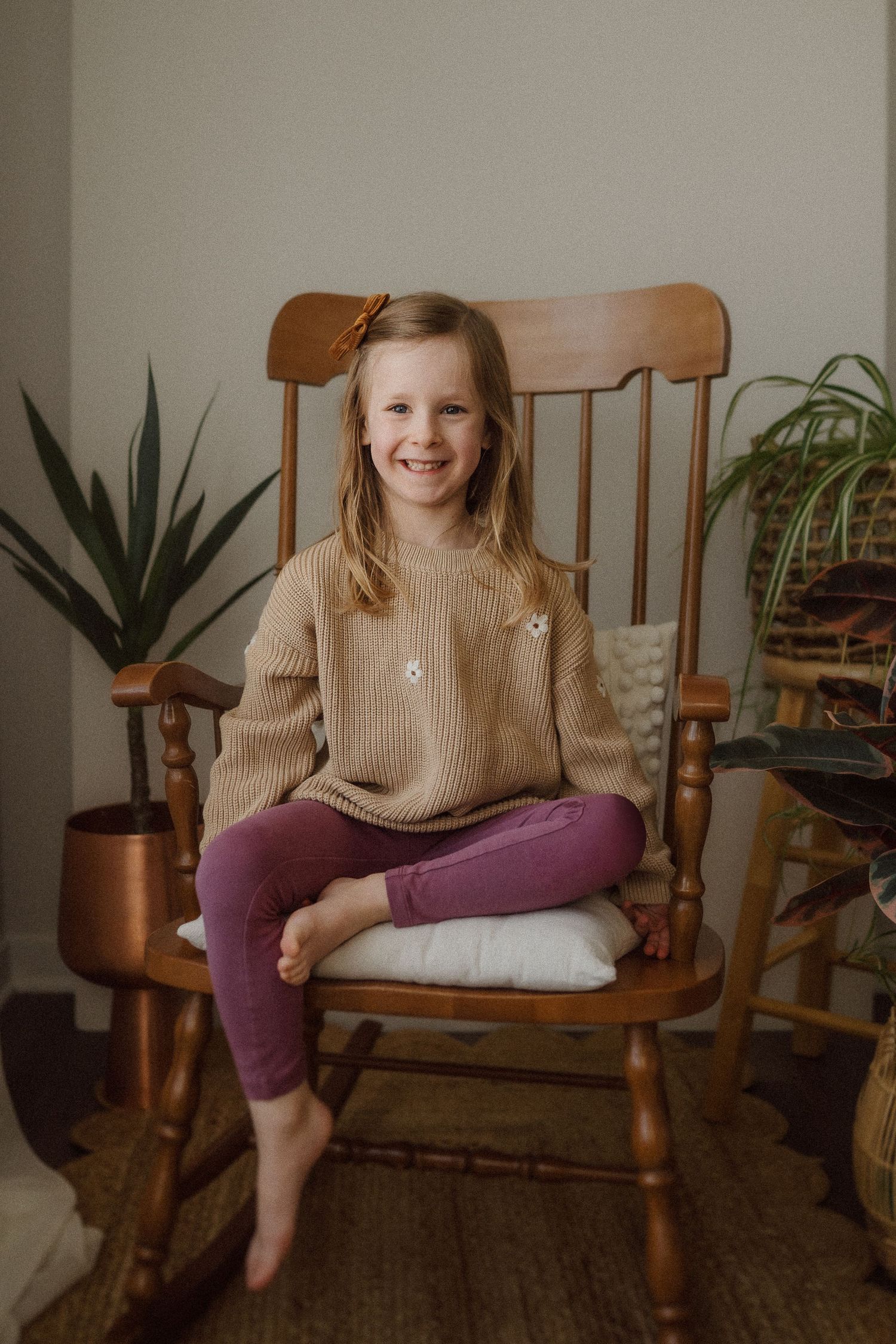 Candid portrait in wooden chair with house plants and copper accents in background.