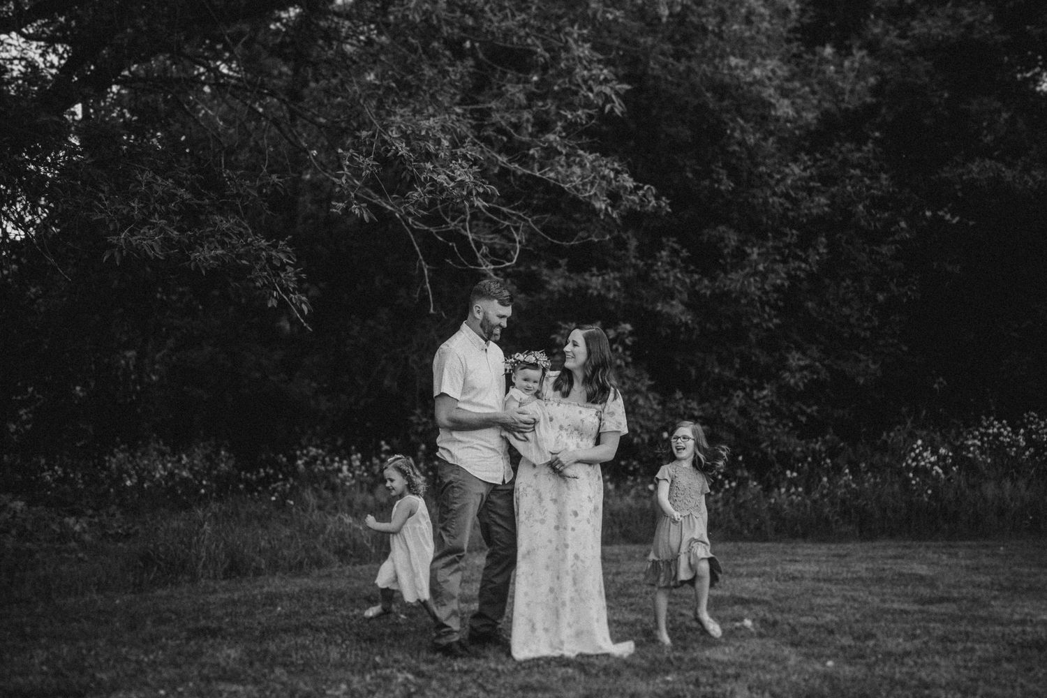 Black and white portrait of a family gathering outdoors in a natural setting.