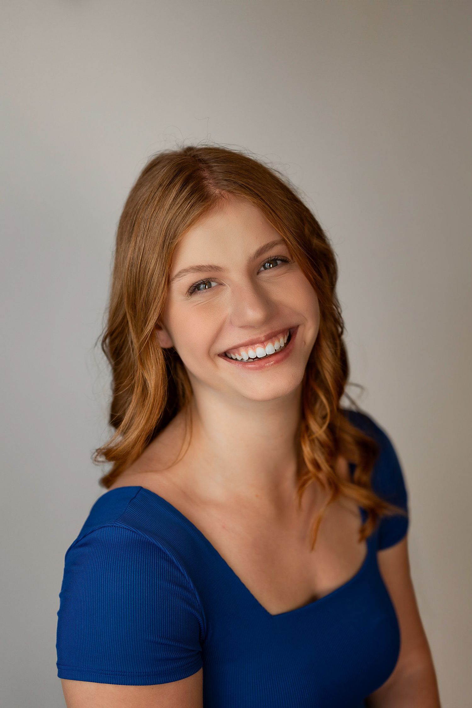Studio portrait of person in blue top with wavy hair against neutral background.