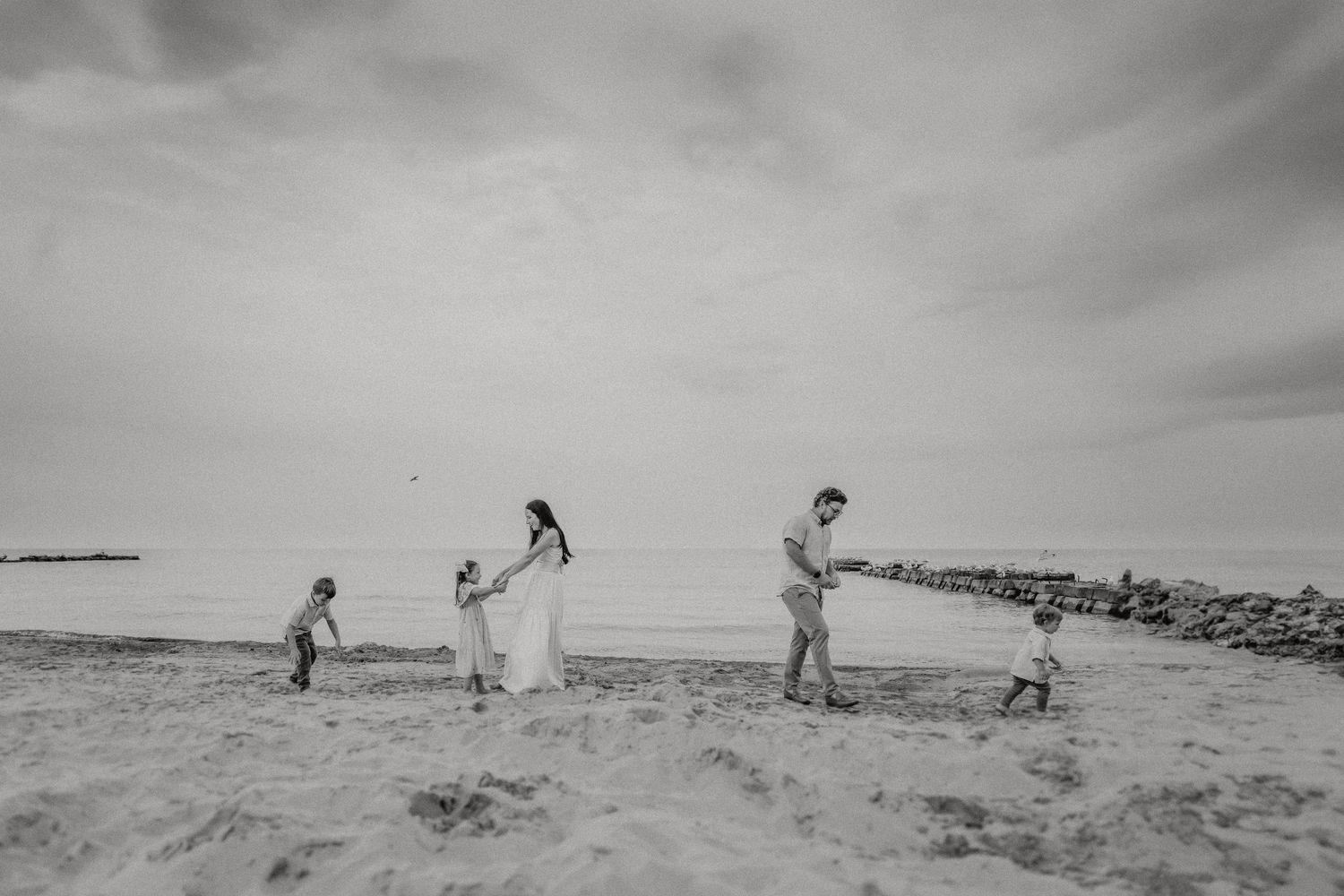 A family plays together on a scenic beach at sunset with a rocky coastline in the background.