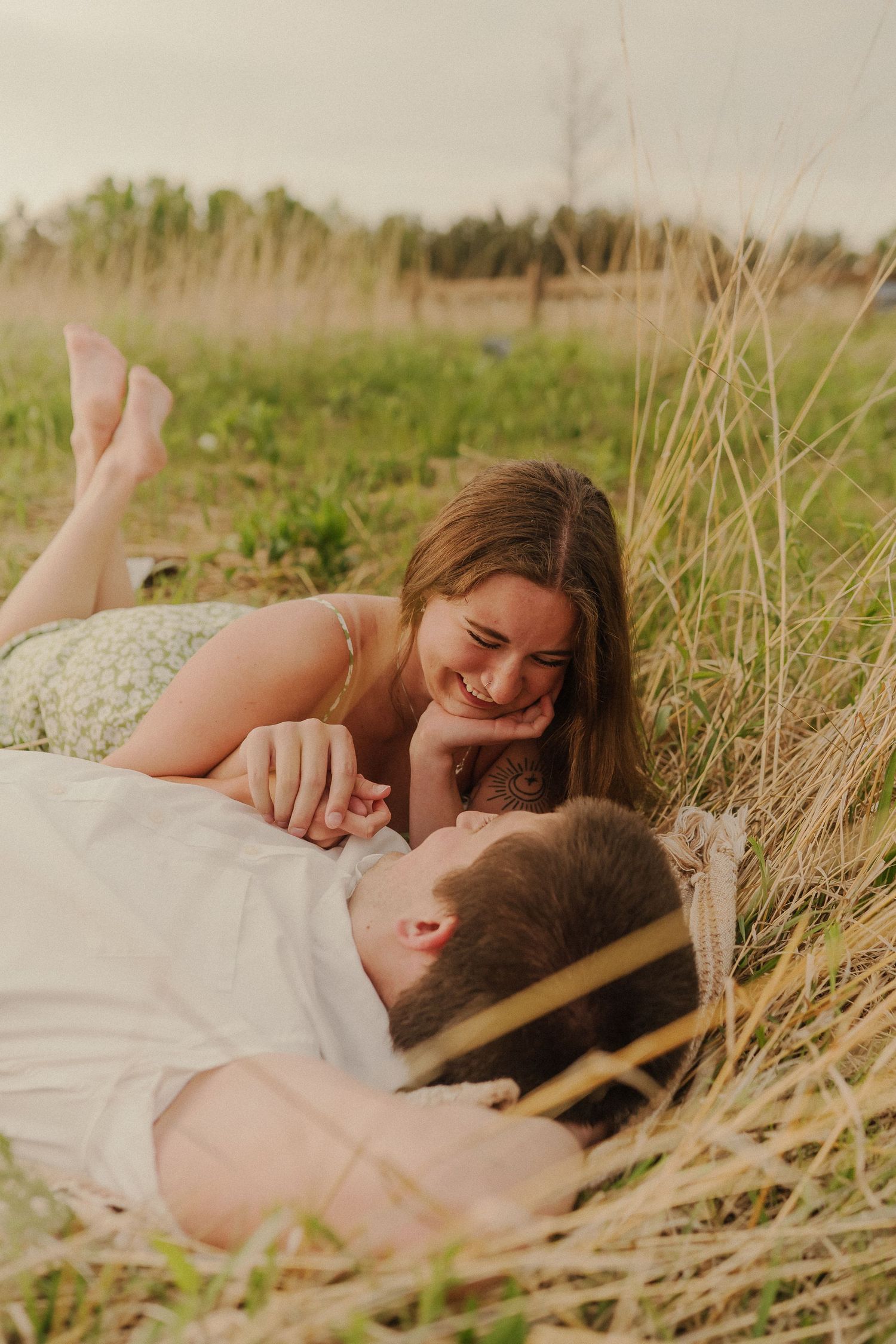 A couple lying in tall grass sharing a joyful, candid moment together.