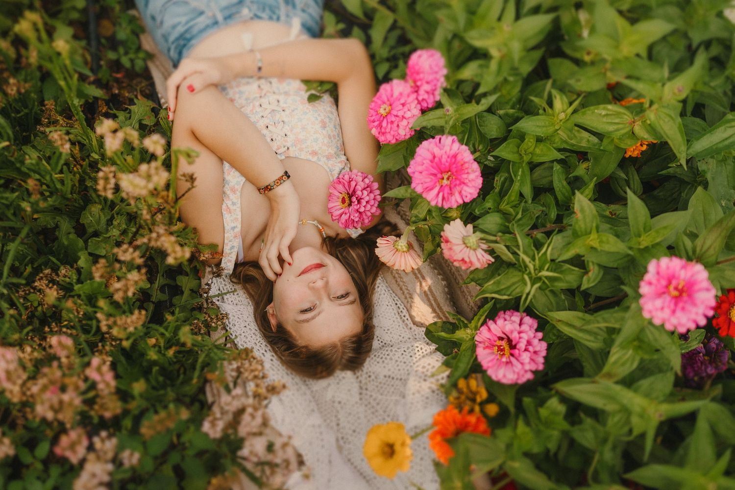 Beautiful white lace dress glows in garden setting surrounded by vibrant pink dahlias and orange flowers.
