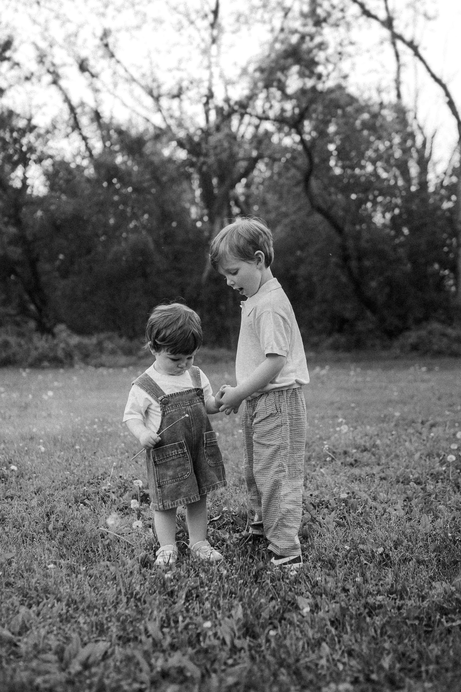 Two children interact while standing in a grassy field in this black and white photograph.