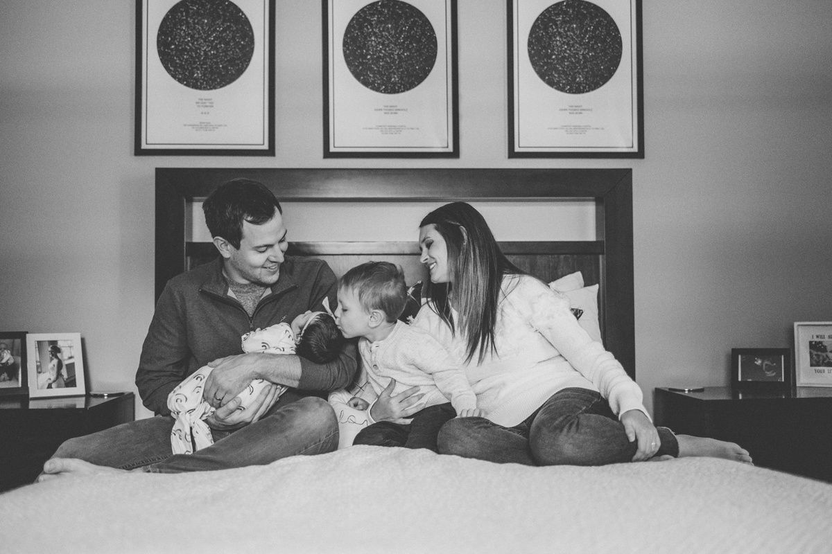 Family relaxing together on bed with black and white moon artwork displayed above.
