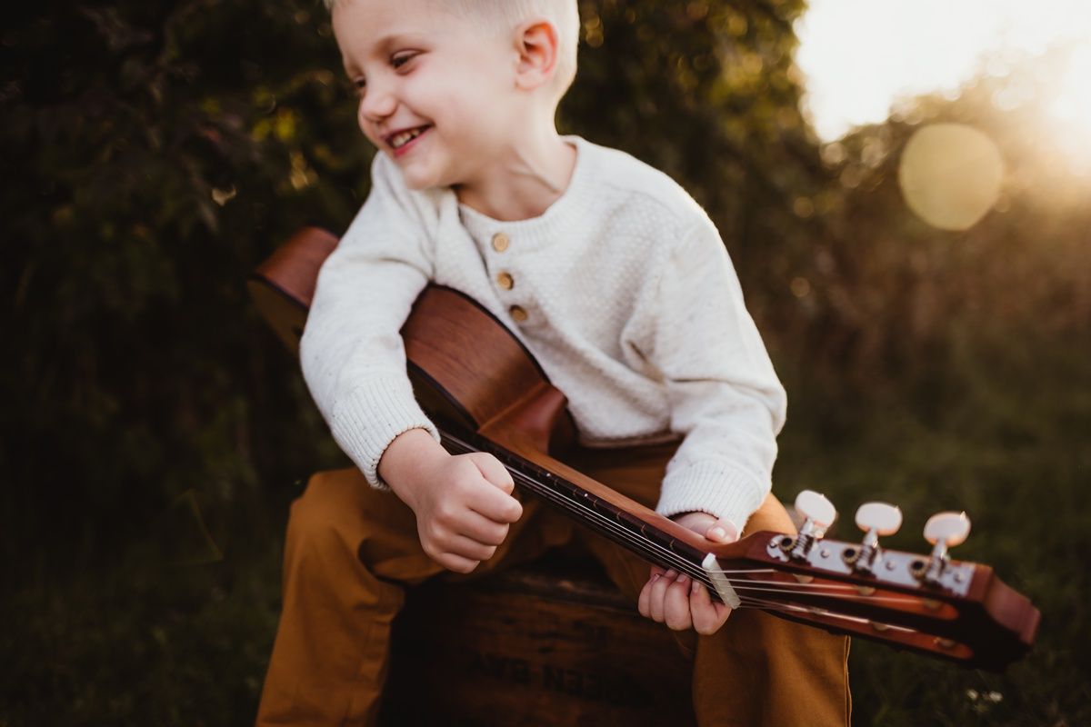 Child joyfully holding and playing with an acoustic guitar in outdoor setting.