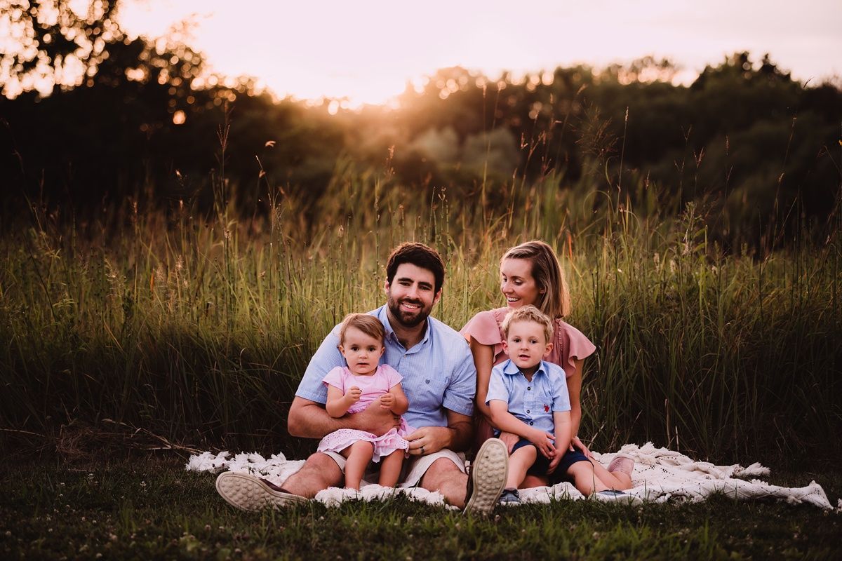 Family sitting together on a blanket in a sunlit meadow during golden hour.