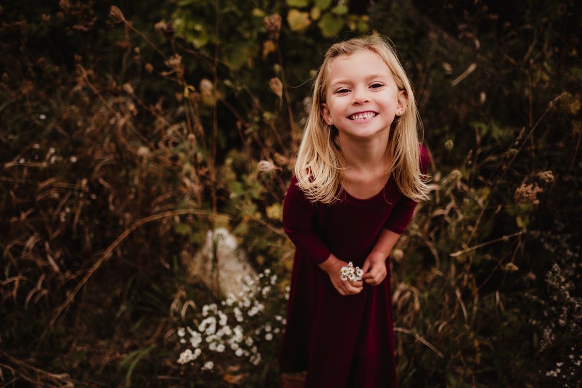 A joyful expression captured in a burgundy dress against an autumn backdrop with white wildflowers.
