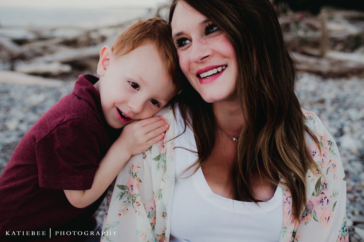 An intimate portrait on a beach with driftwood featuring warm smiles and casual attire.