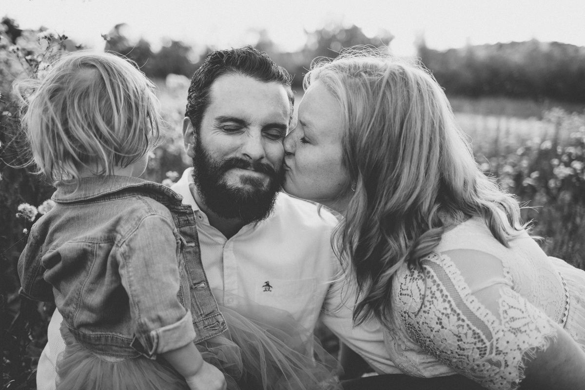 Black and white portrait of a family sitting together in a wildflower field.